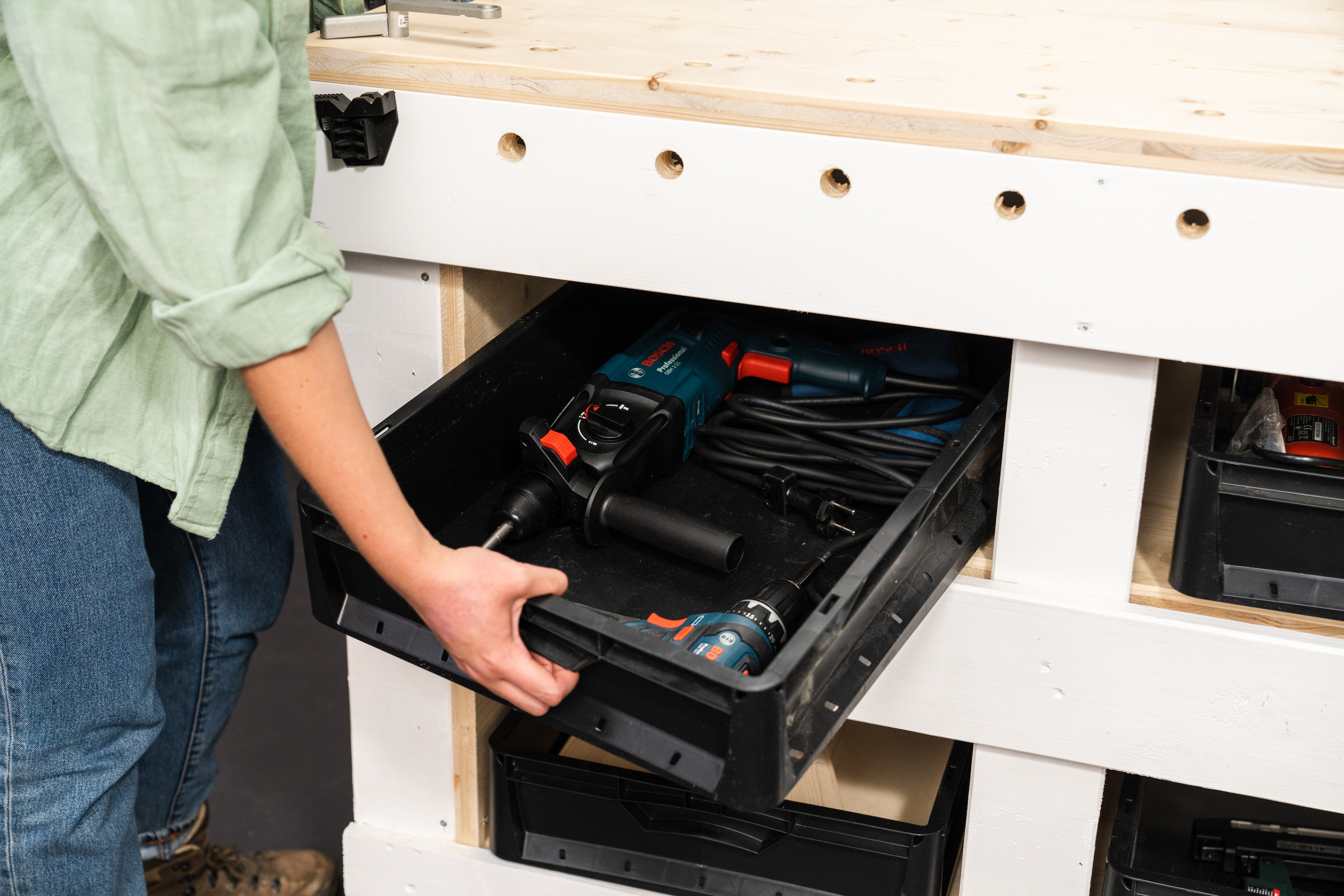 Egy nő kivesz egy doboz szerszámot a munkapadból.