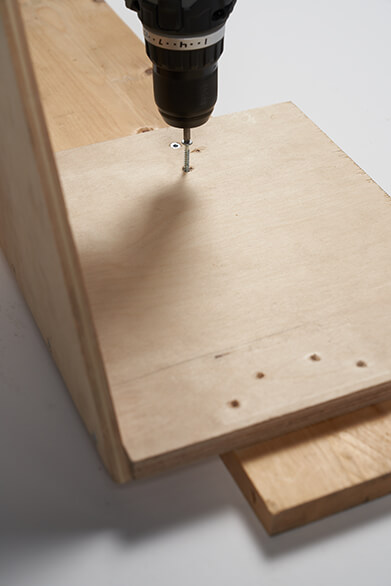 Egy személy akkus csavarhúzóval lyukakat fúr egy fából készült panelbe.