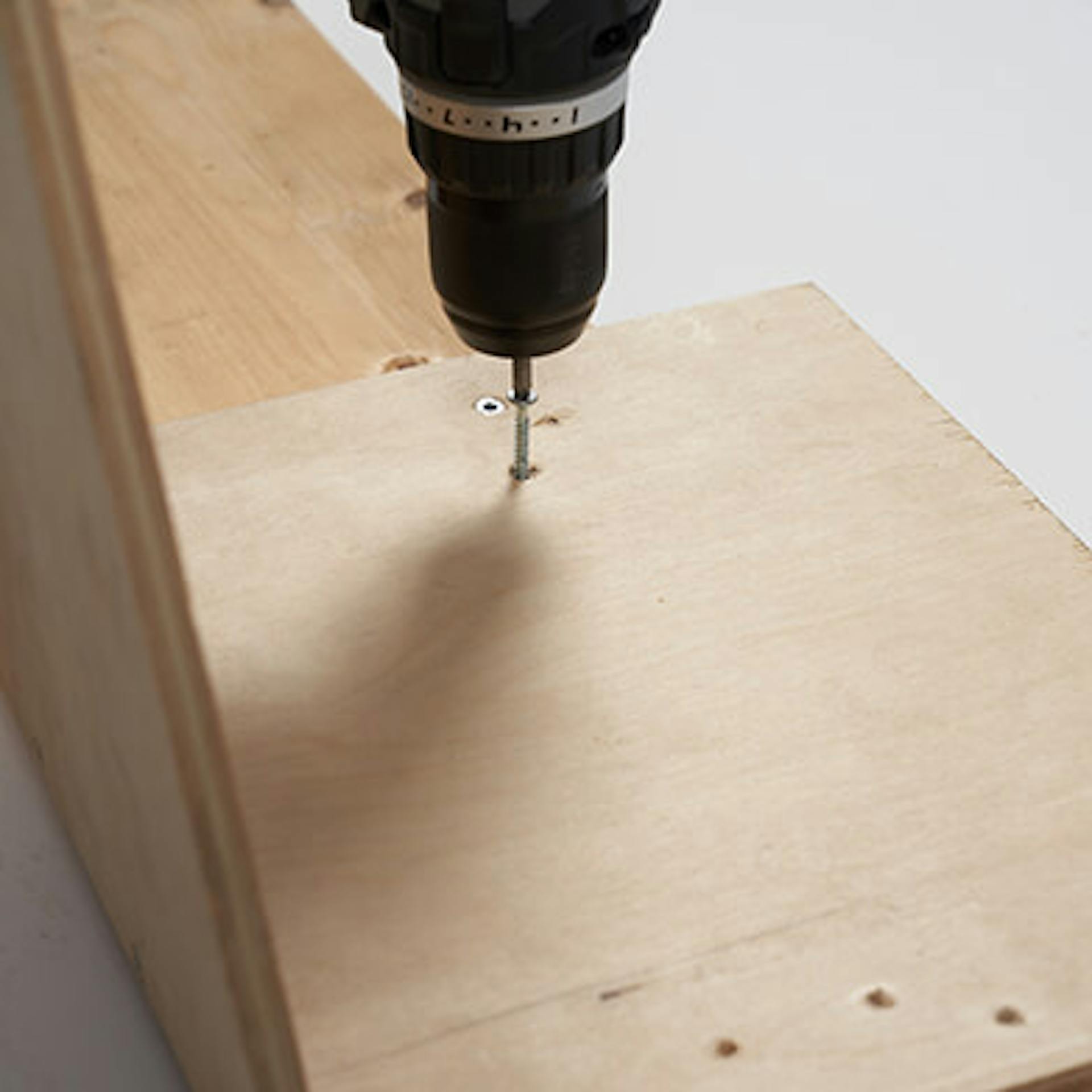 Egy személy akkus csavarhúzóval lyukakat fúr egy fából készült panelbe.