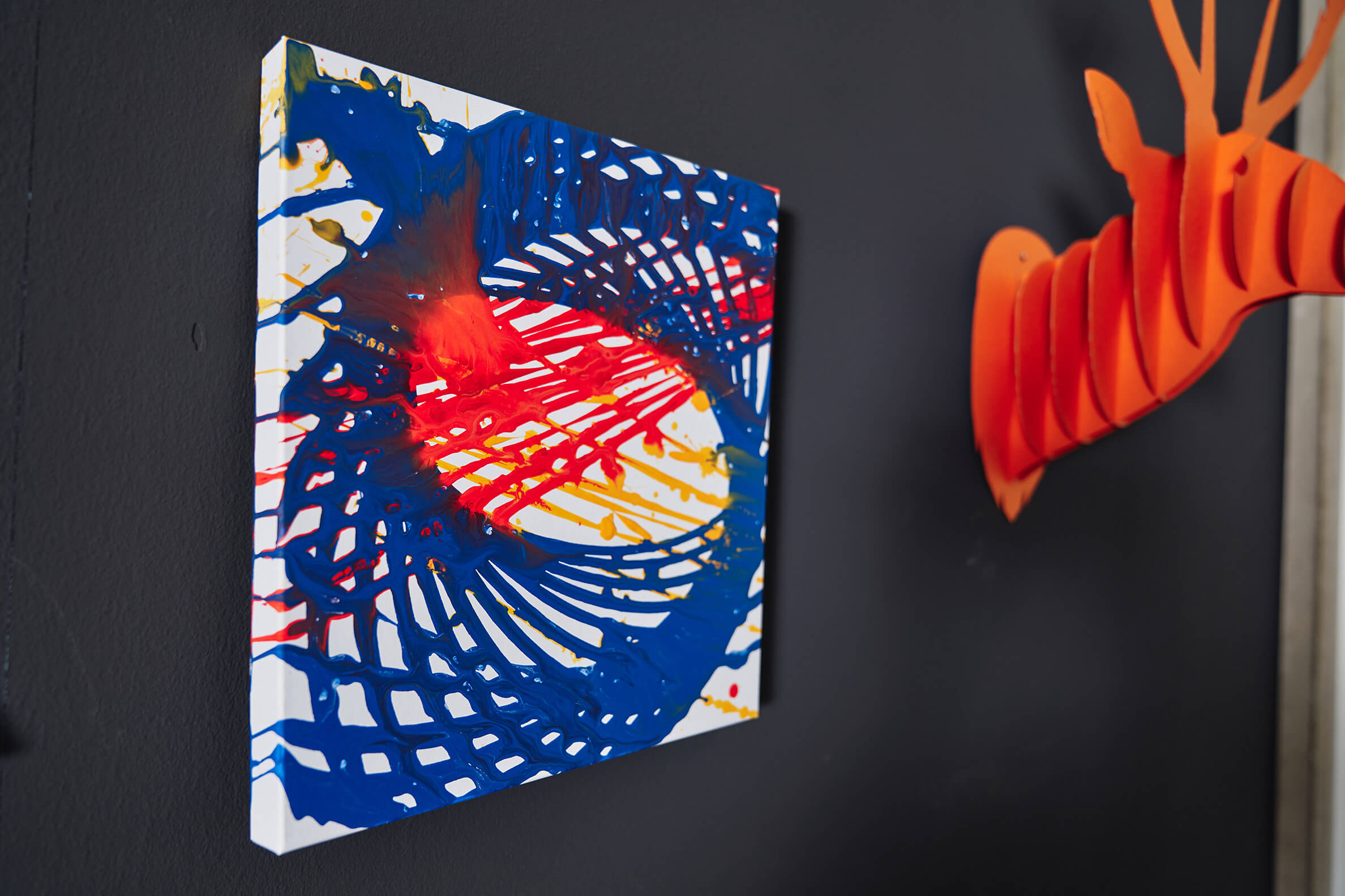 Ein Pendel-Bild hängt an einer grauen Wand, daneben ein orangener Hirschkopf aus Pappe