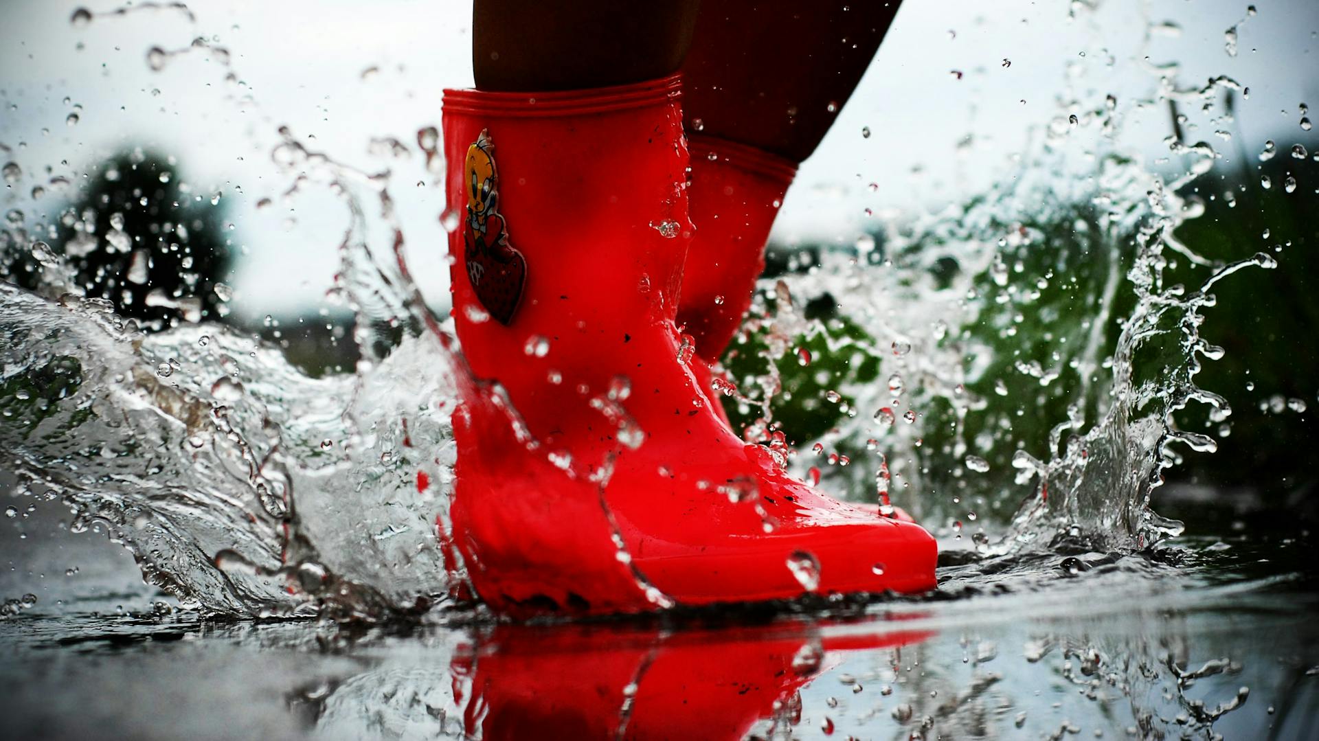 Sprung in Pfütze mit roten Gummistiefeln