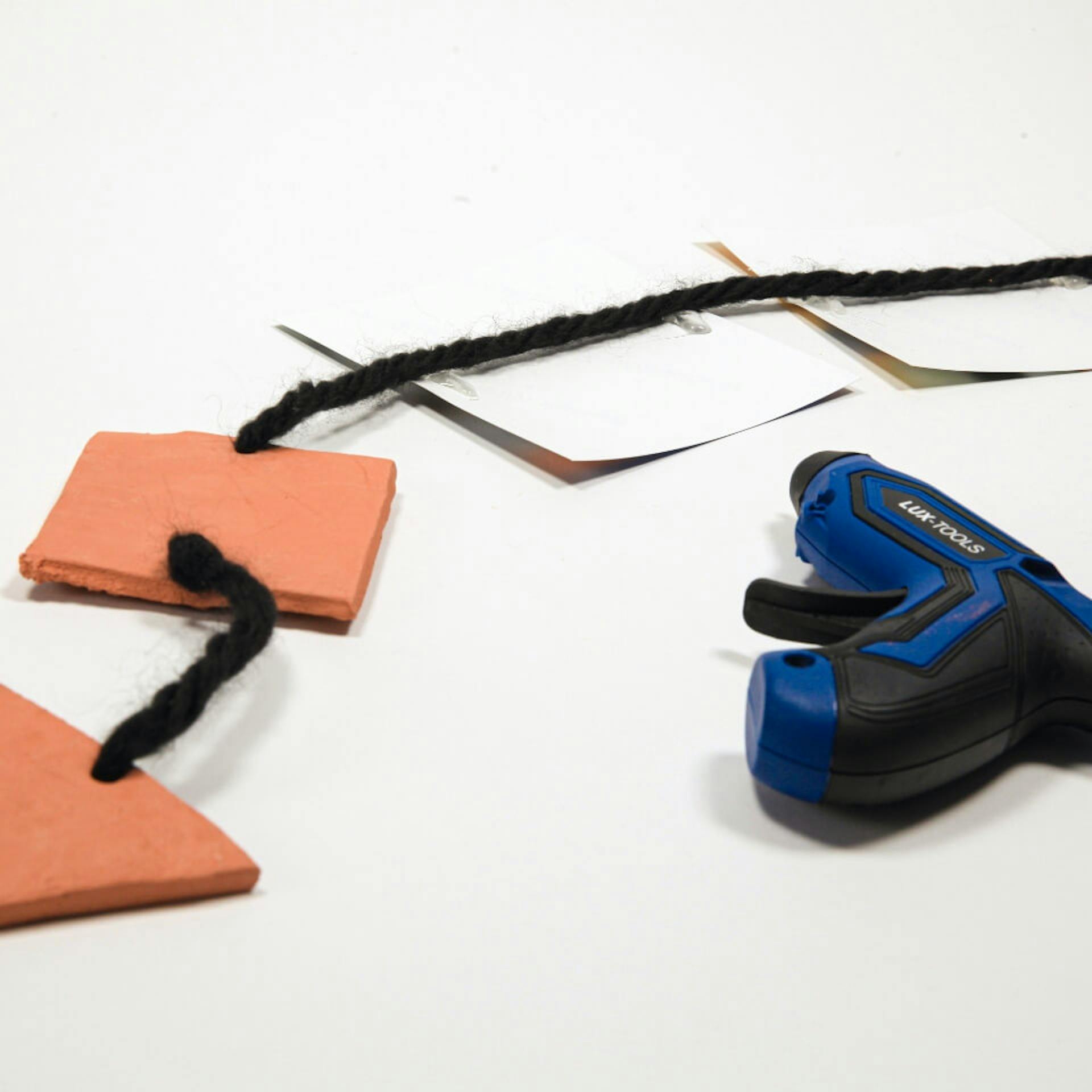 Heißklebepistole liegt neben Schnur, an der Tonformen und Fotos befestigt sind