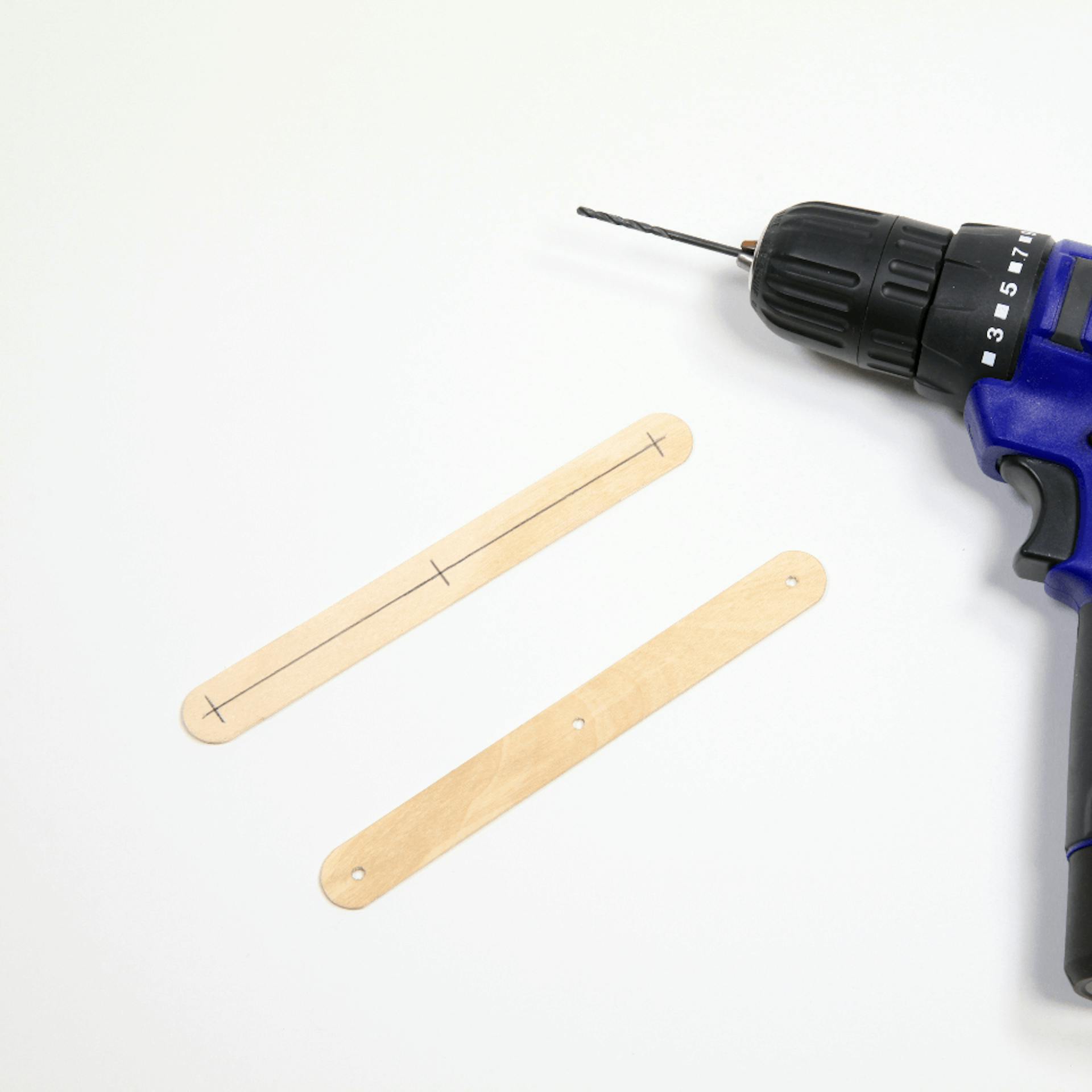Zwei Holzstücke, auf dem einen ist mittig eine Linie eingezeichnet und drei Punkte. Daneben liegt ein Akkuschrauber.