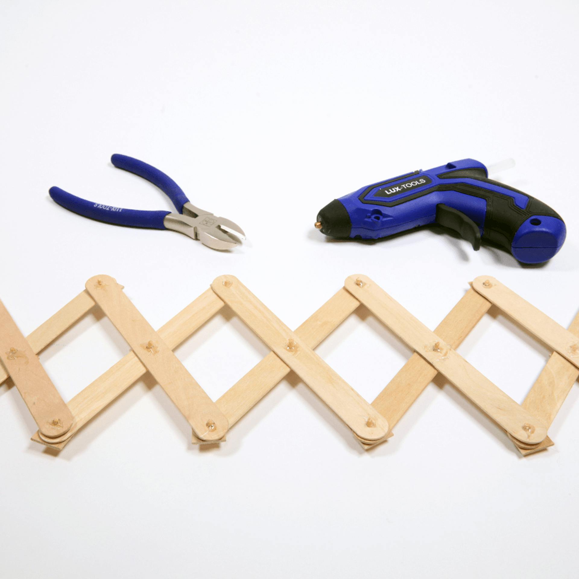 Scherengelenk aus Holz, darüber eine Zange und eine Heißklebepistole.