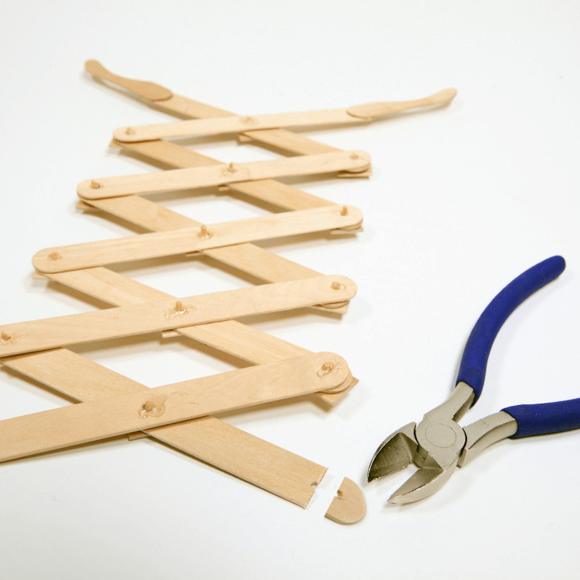 Zange liegt neben zusammenmontierten Gelenken des Greifarms, dazwischen liegt ein abgeschnittenes Stück Holz.