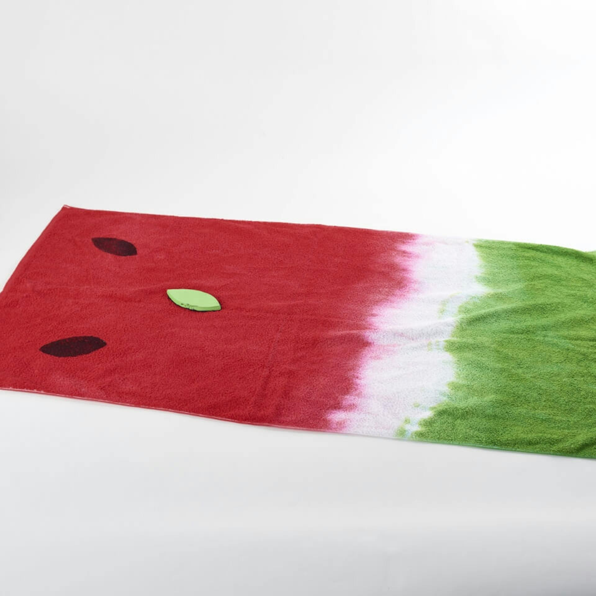 Es ist ein ausgebreitetes Handtuch zu sehen.Eine Seite ist rot gefärbt, die andere grün. Ein kleiner Teil des Handtuchs ist weiß. Auf dem roten Bereich des Handtuchs sind zwei schwarze Abdrücke zu sehen. Daneben liegt eine grüne Moosgummiform.