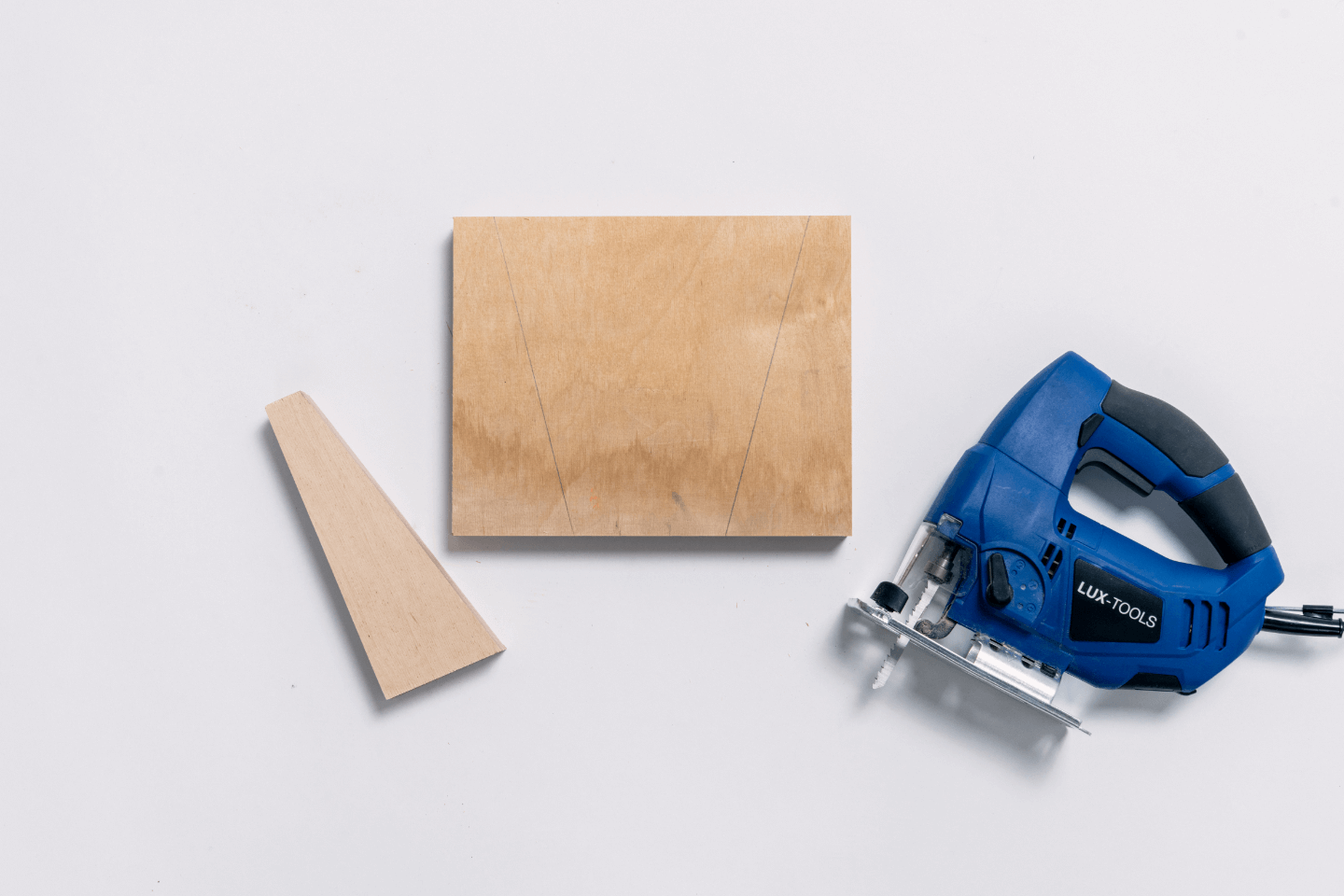 Neben einer Holzplatte liegt ein ausgesägter Keil. Daneben liegt die Stichsäge.