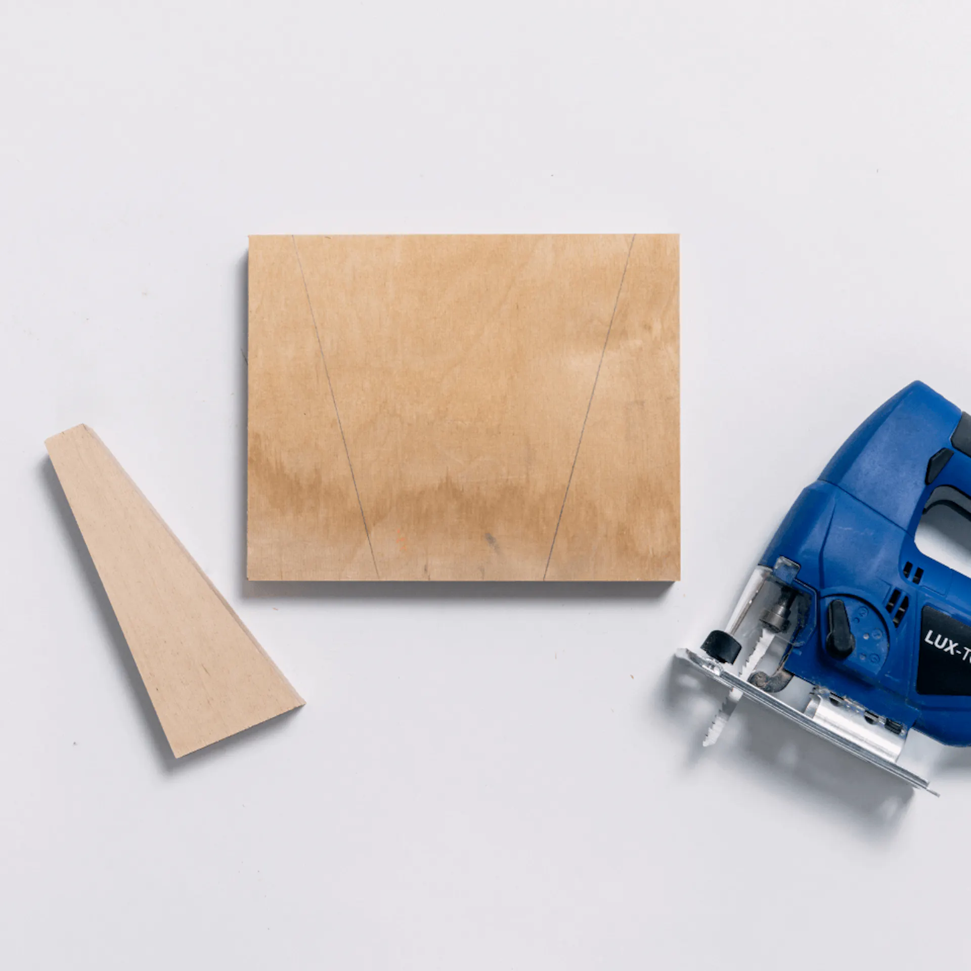 Neben einer Holzplatte liegt ein ausgesägter Keil. Daneben liegt die Stichsäge.