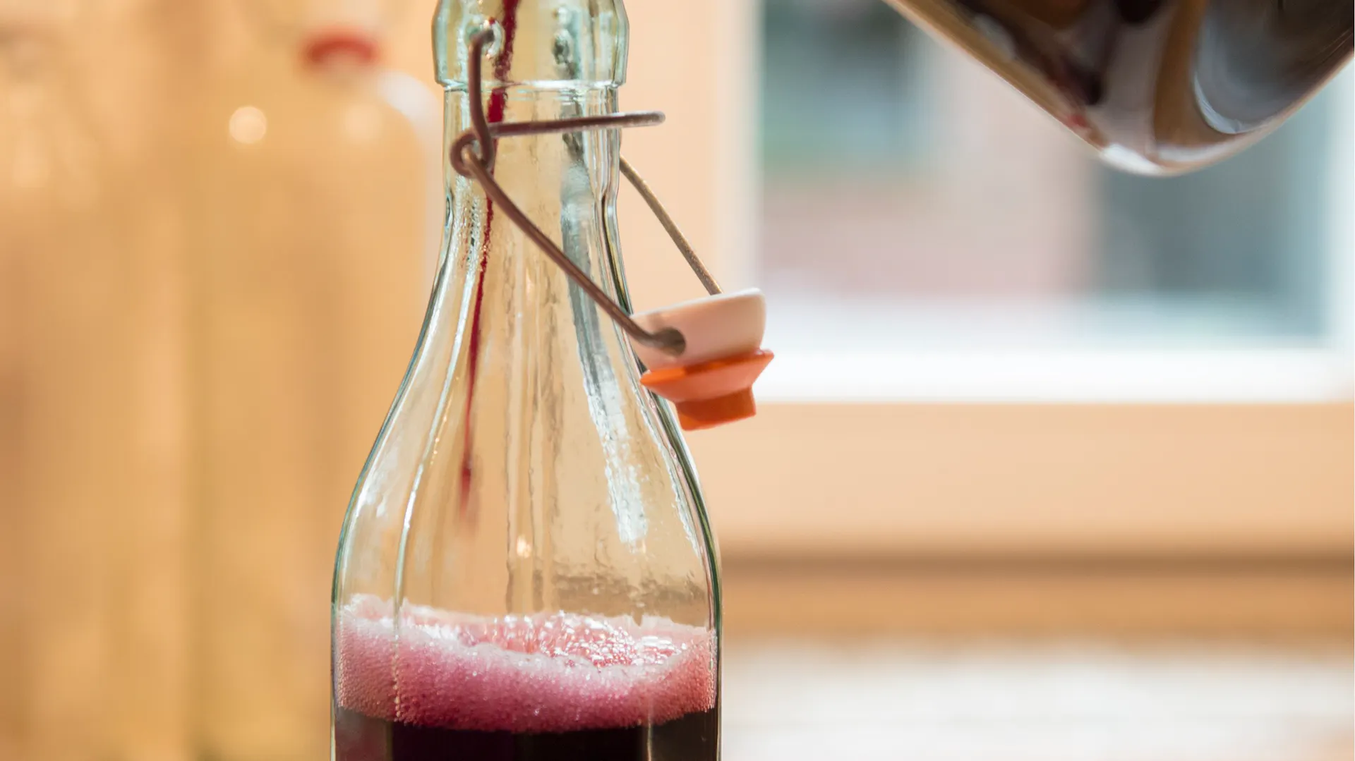Jemand gießt heißen Holundersaft in eine Glasflasche.