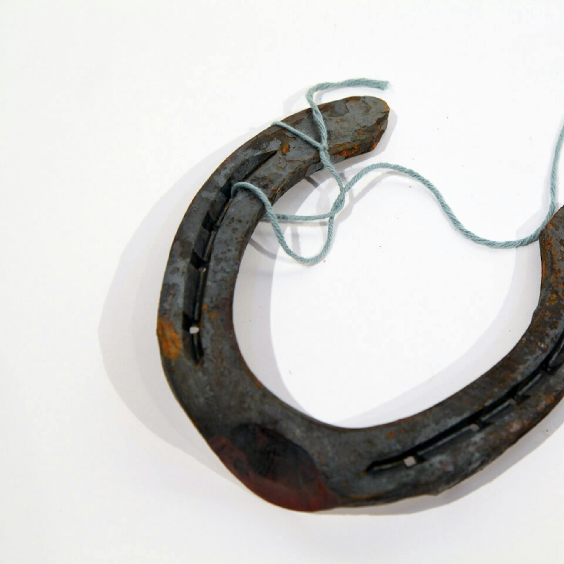 Faden durchgefädelt durch zwei Löcher eines Hufeisens.