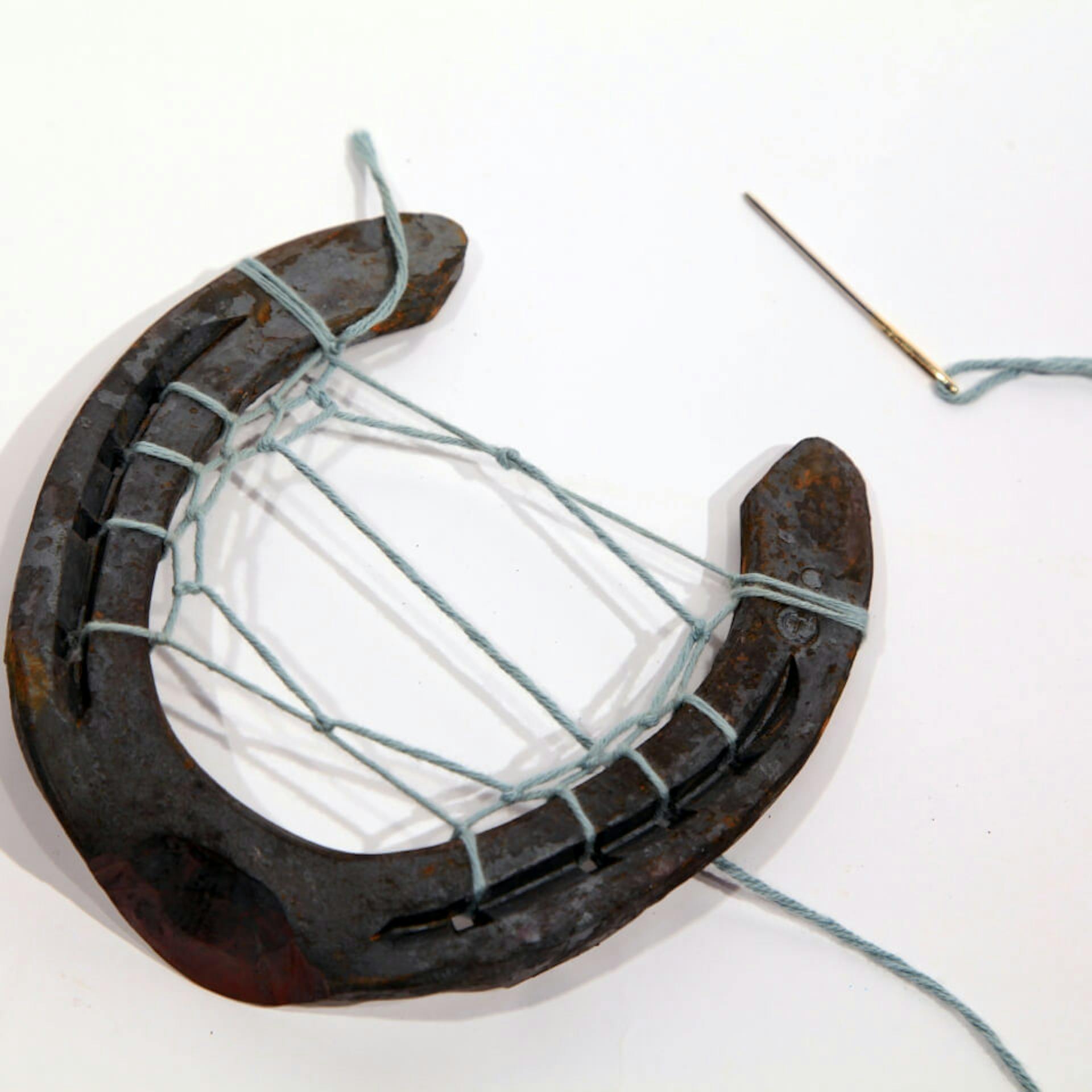 Nadel und ein Faden, der durch ein Hufeisen gefädelt und verknotet wurde.