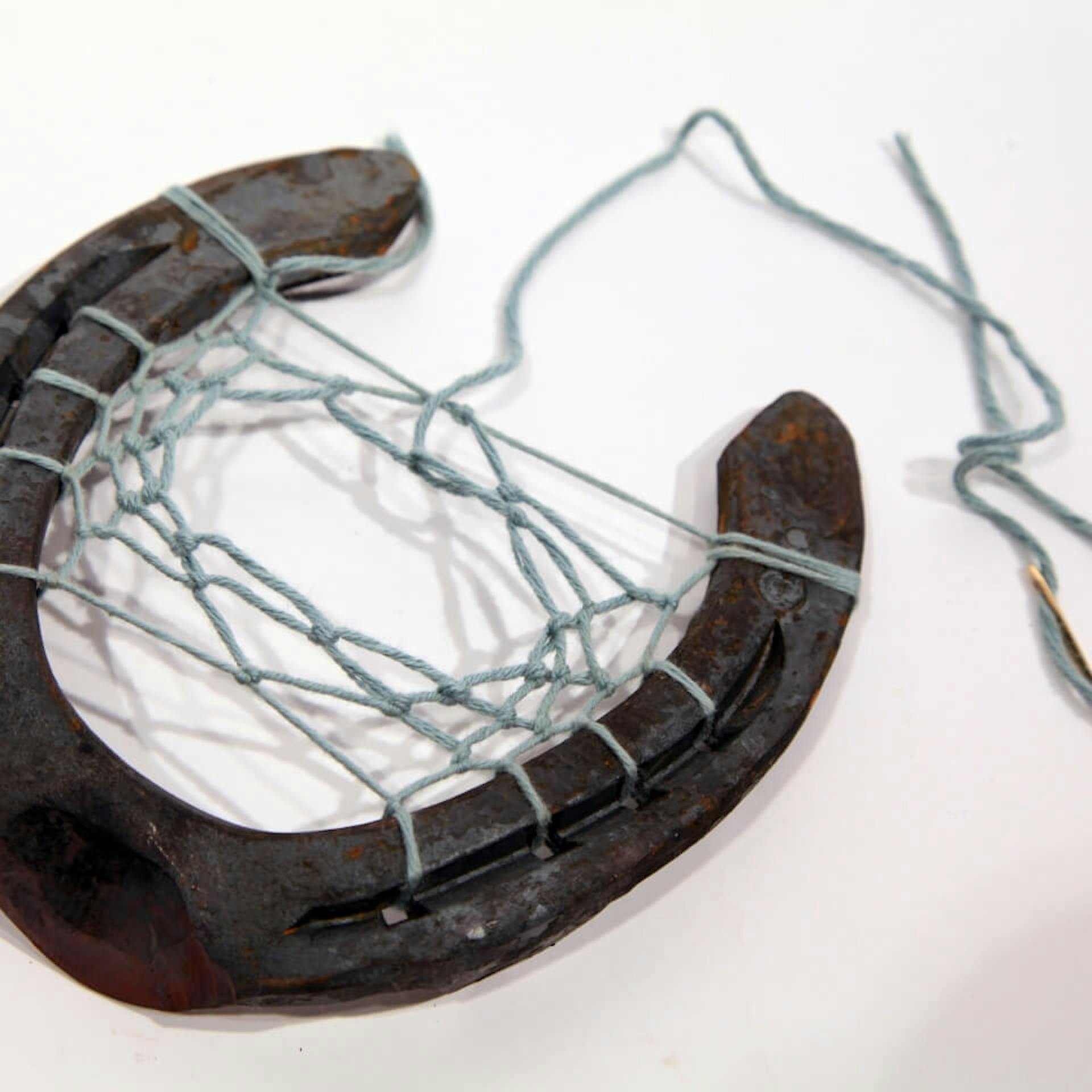 Nadel und ein Faden, der kreuz und quer durch ein Hufeisen gefädelt und verknotet wurde.