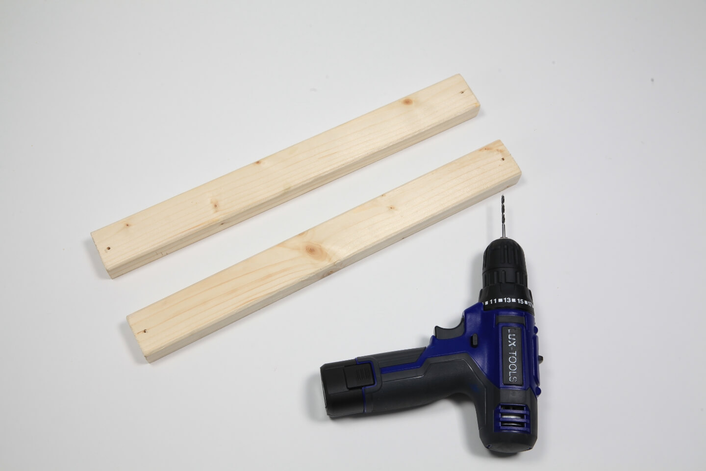 Zwei Holzlatten und ein Akkuschrauber liegen auf einem Tisch.