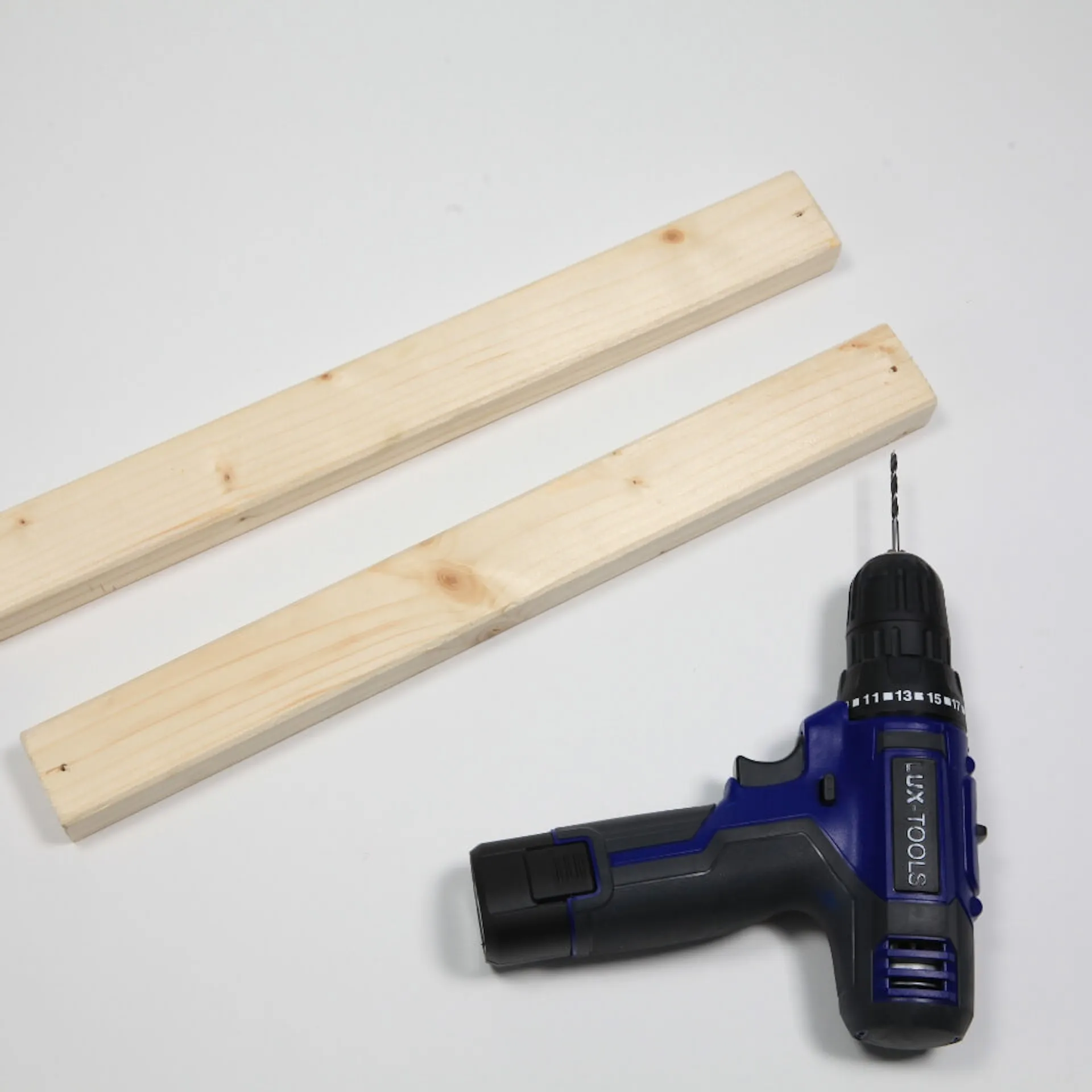 Zwei Holzlatten und ein Akkuschrauber liegen auf einem Tisch.