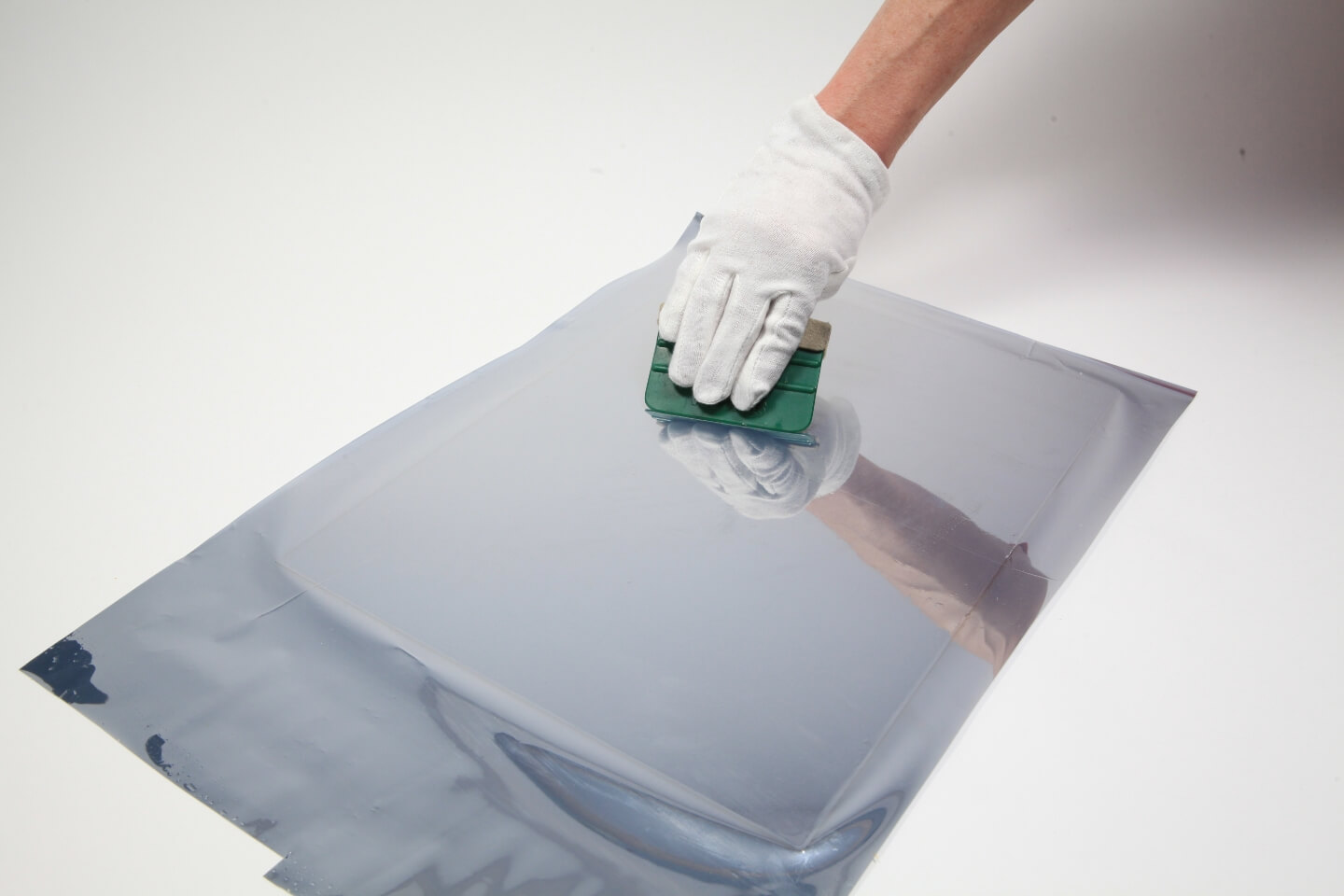 Eine Person entfernt mit einem Rakel Lufteinschlüsse zwischen Plexiglas und Spiegelfolie.