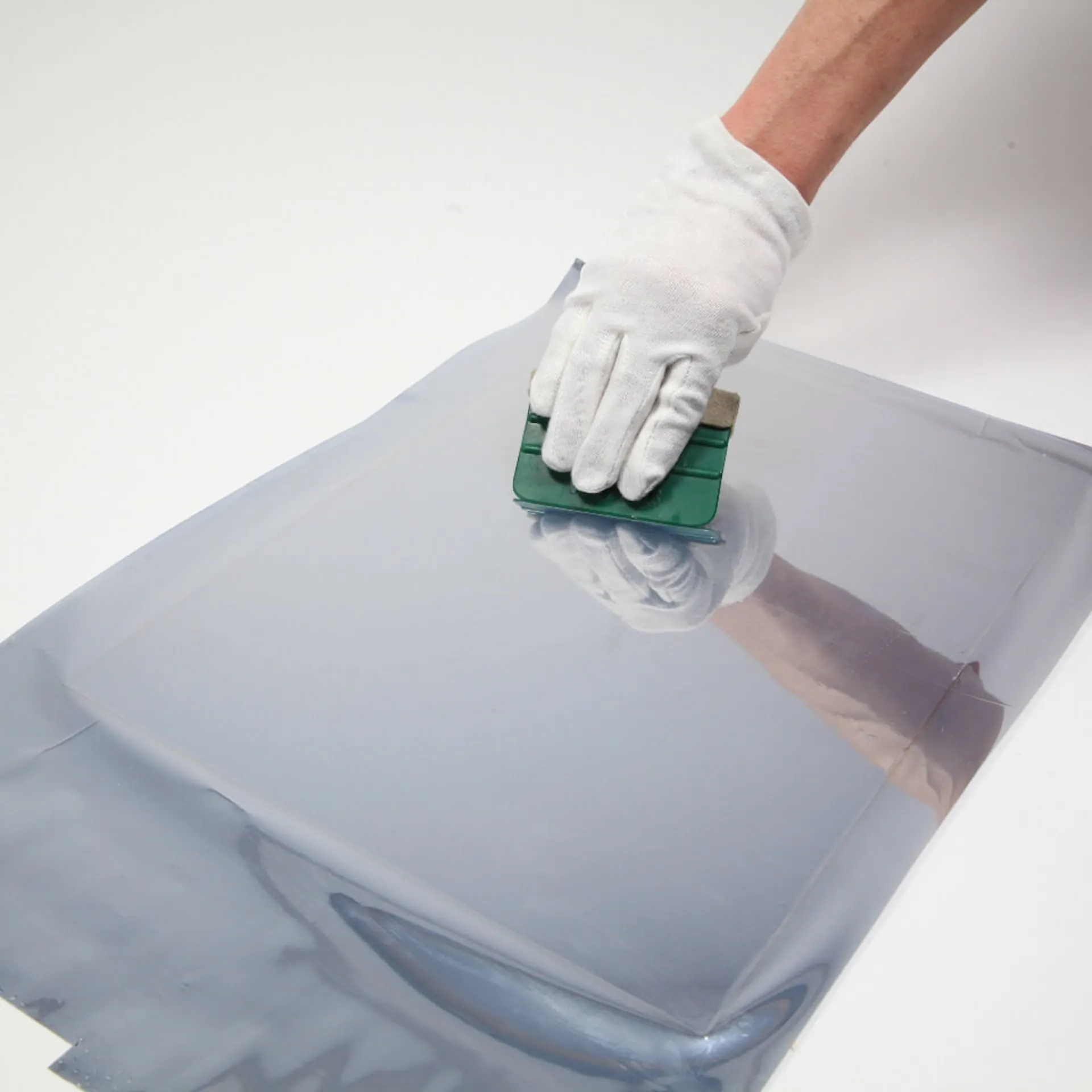 Eine Person entfernt mit einem Rakel Lufteinschlüsse zwischen Plexiglas und Spiegelfolie.