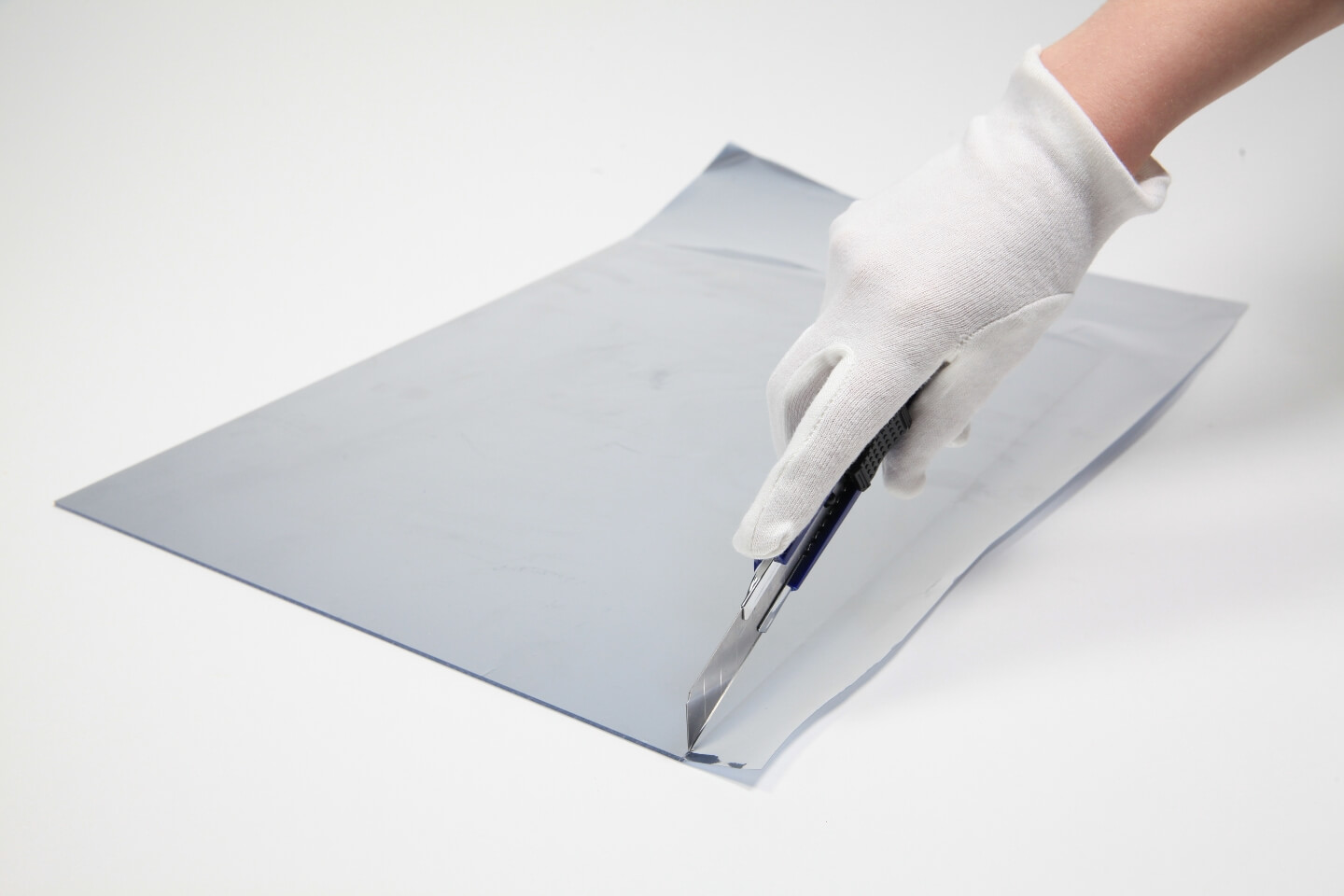 Eine Person schneidet mit einem Cutter die Überstände der Spiegelfolie ab.