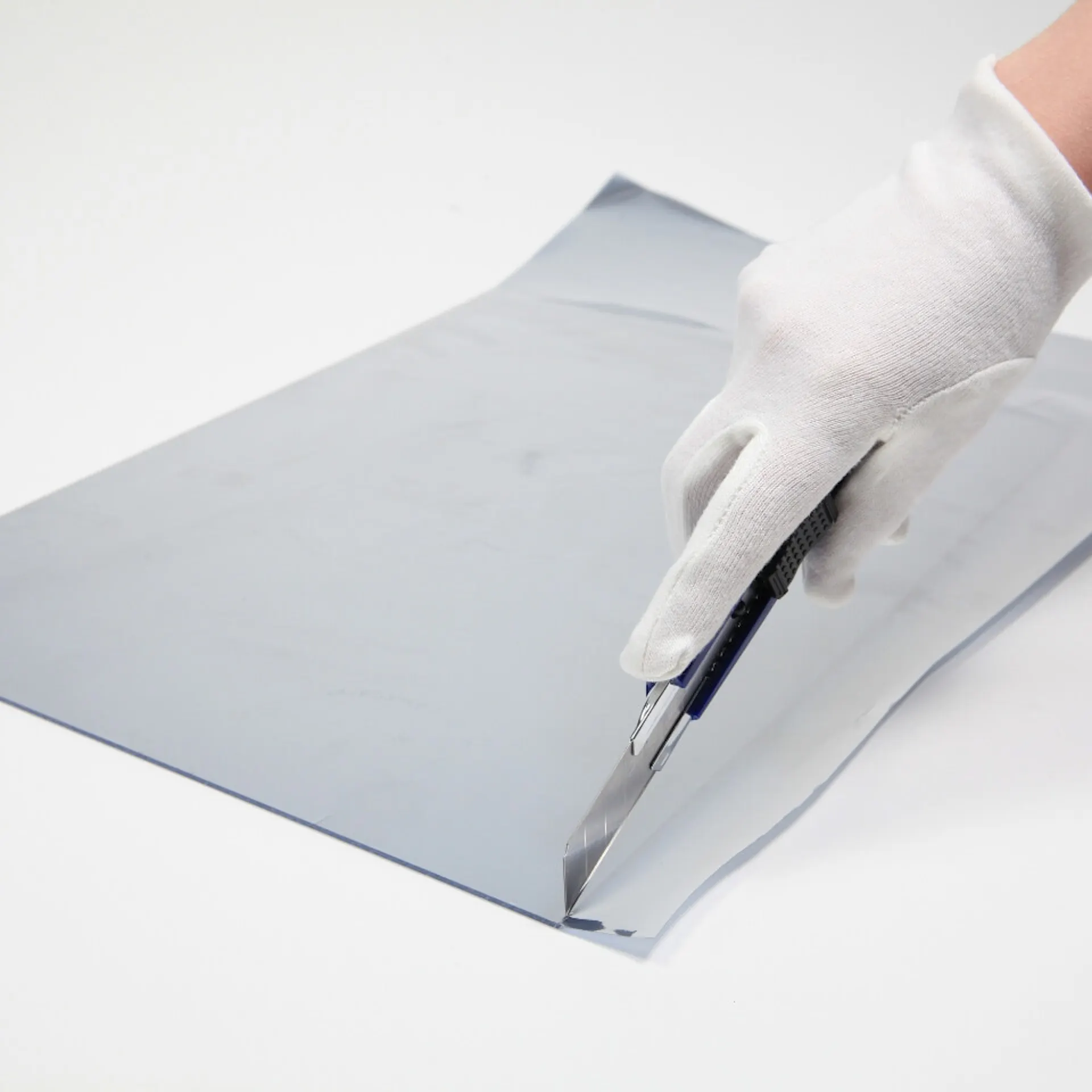 Eine Person schneidet mit einem Cutter die Überstände der Spiegelfolie ab.
