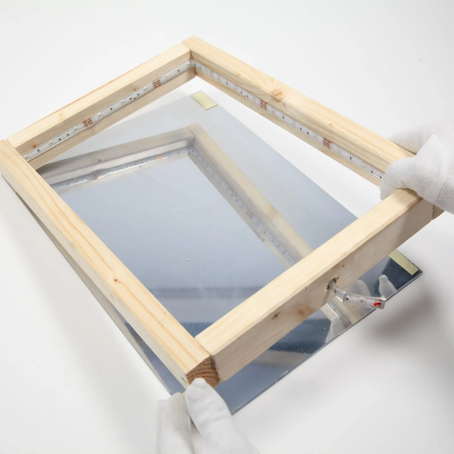 Eine Person drückt den Holzrahmen auf das Plexiglas mit der Spiegelfolie.
