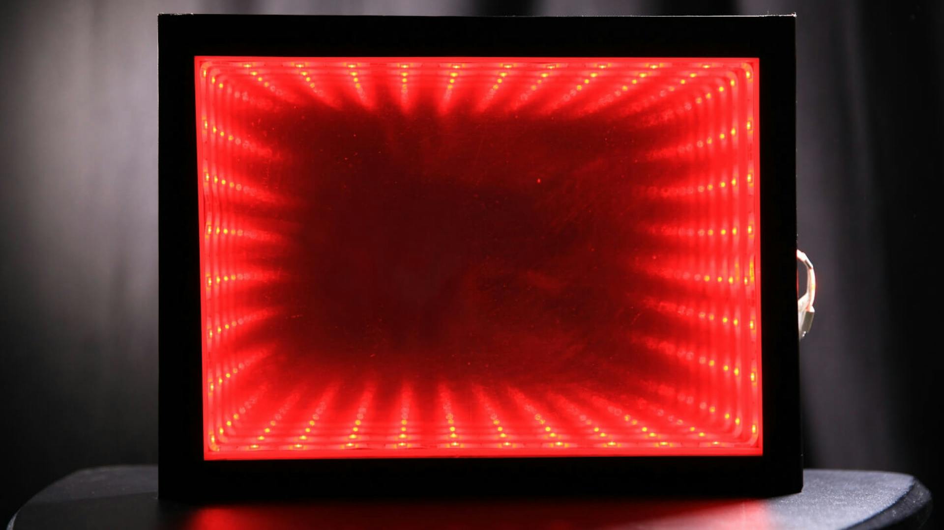 Ein Infinity Mirror mit roter Beleuchtung steht auf einem Tisch.