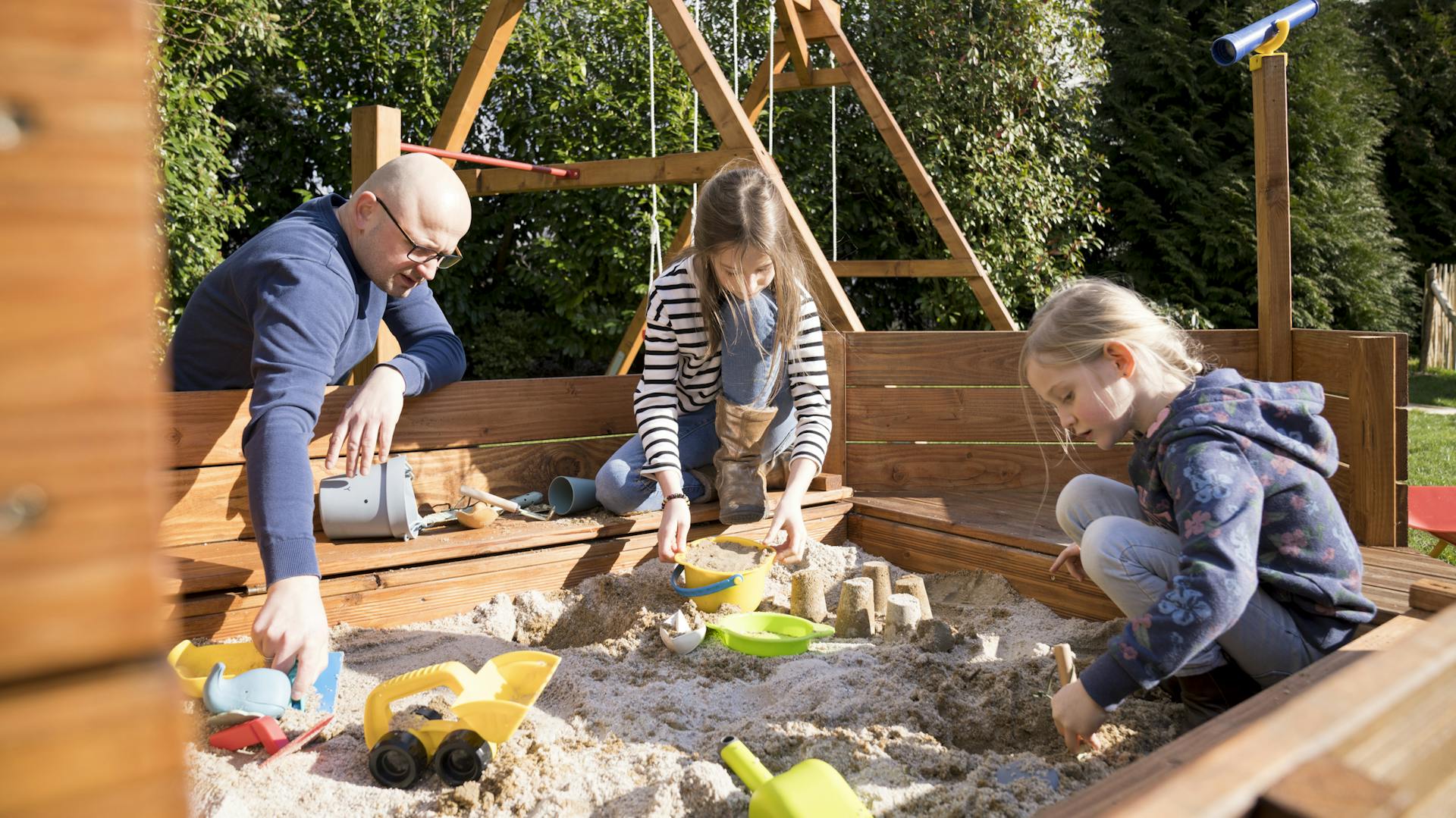 Töchter mit Vater spielen im Sandkasten