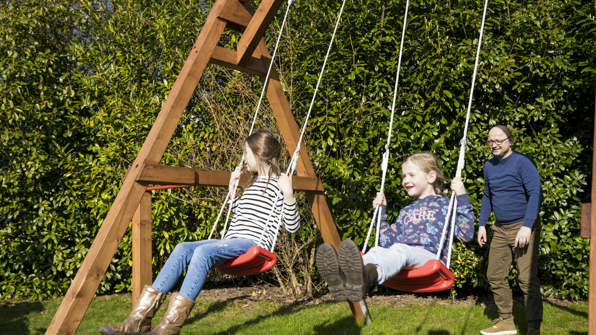 Zwei Töchter schaukeln mit ihrem Vater im Garten