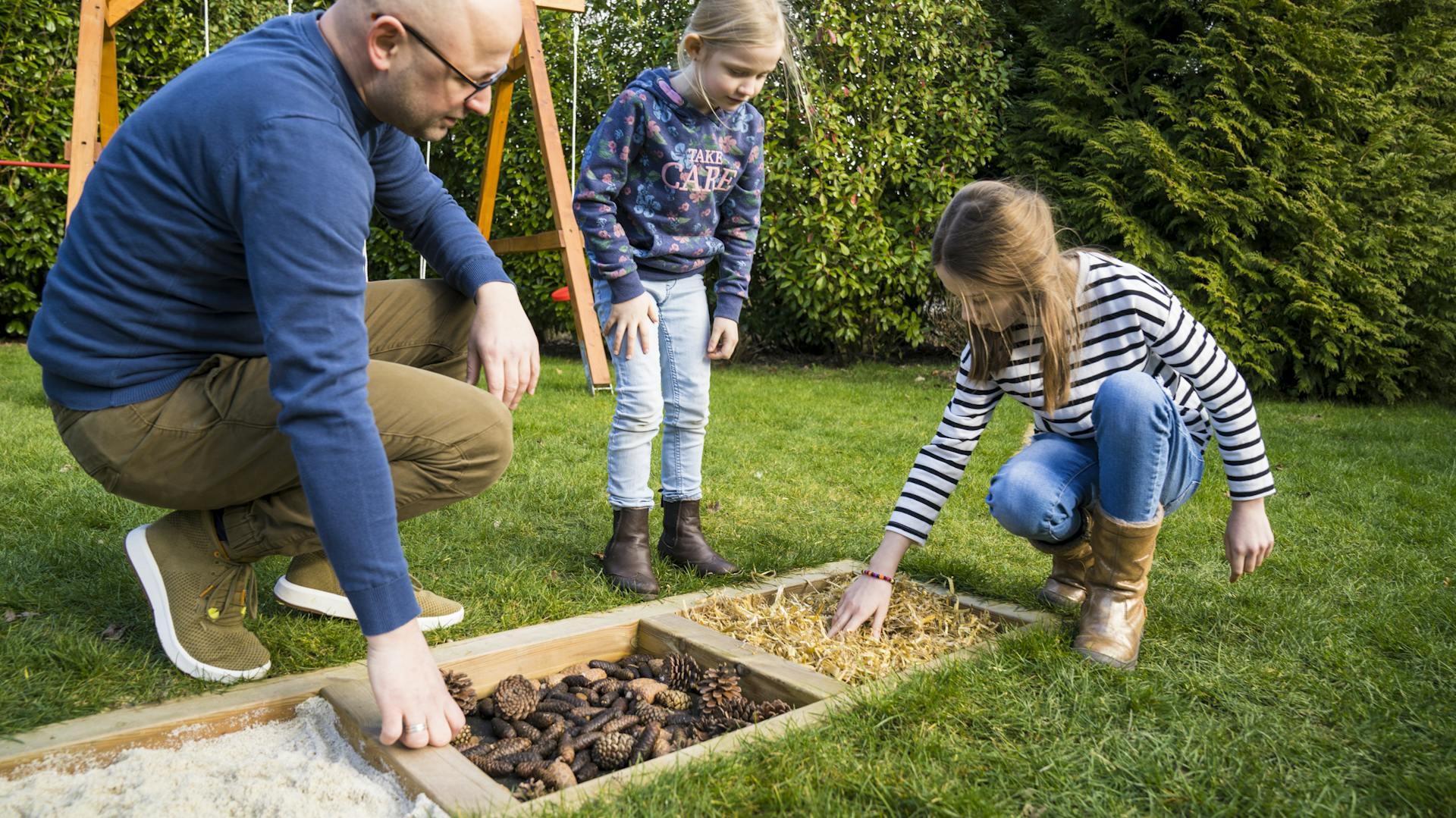 Vater zeigt Töchtern die Materialien des Barfußpfades