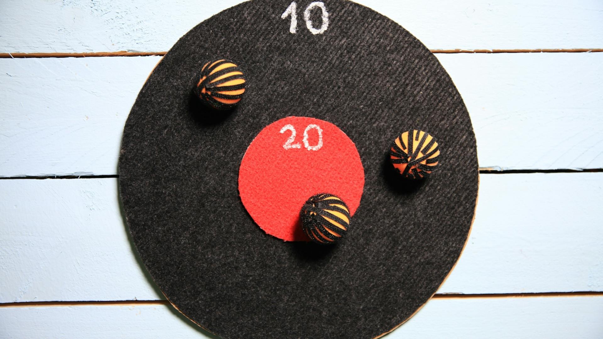 Dartscheibe aus Klett mit Bällen und Zahlen hängt an Wand.