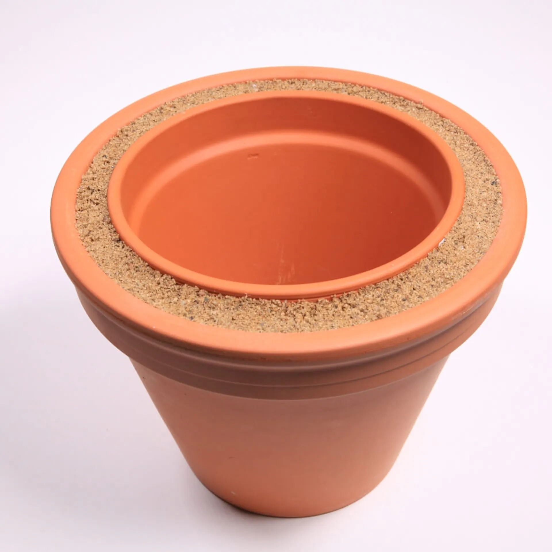 Im Zwischenraum zwischen den beiden Tontöpfen befindet sich Sand.