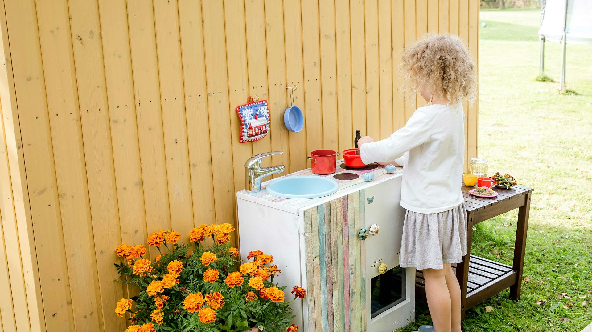Ein Mädchen spielt mit einer Matschküche im Garten