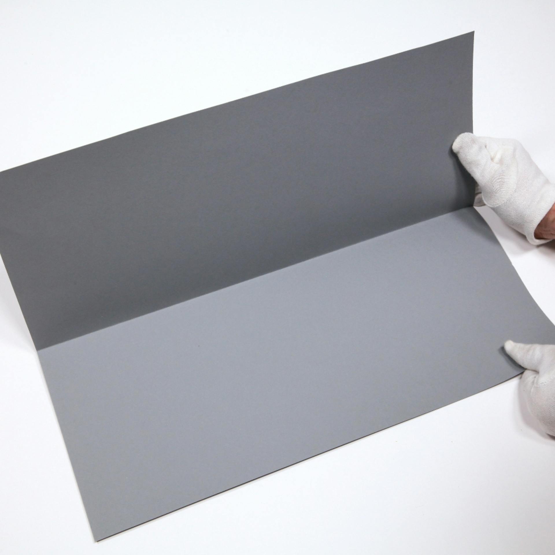 Eine Person mit Handschuhen faltet ein graues Stück Pappe in der Mitte.