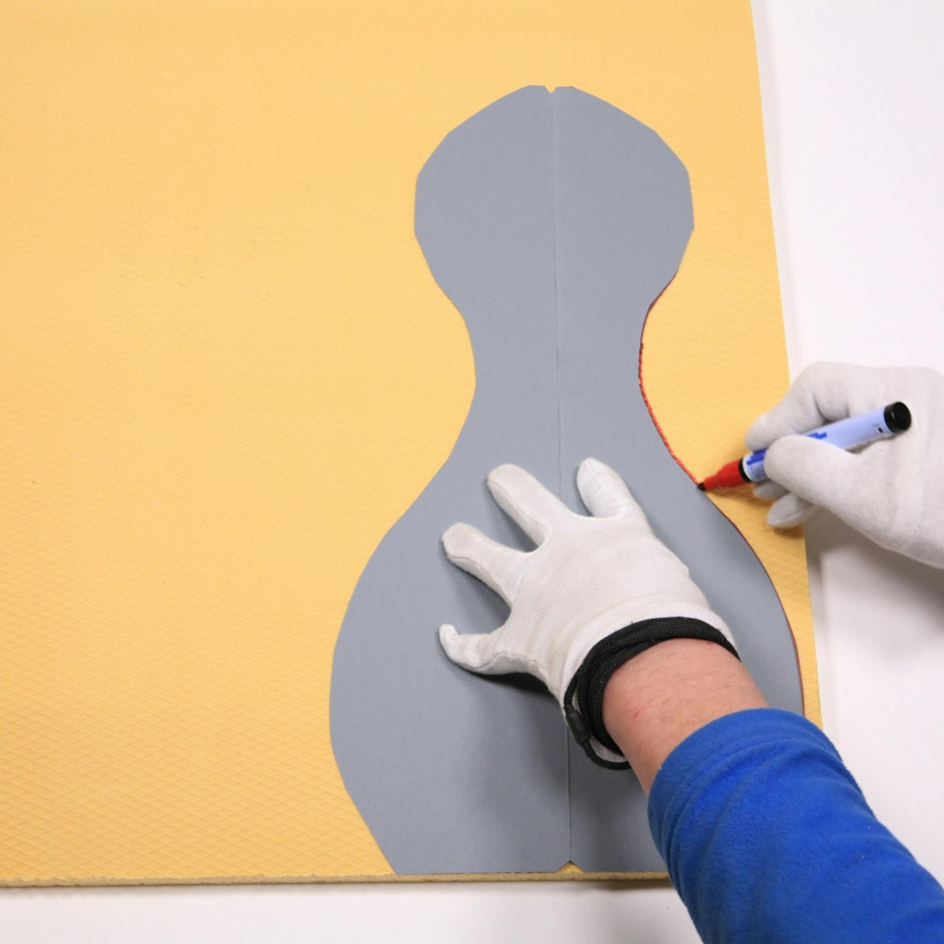 Jemand zeichnet die Umrisse eines Bowling-Pins auf einer Dämmplatte nach.