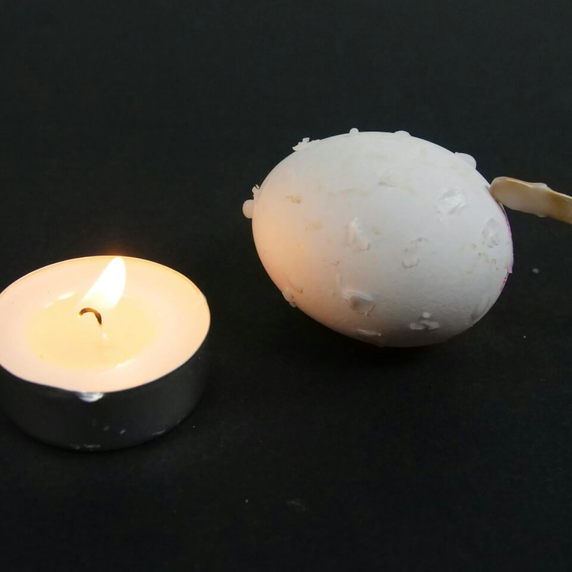 Un uovo decorato con cera di candela accanto a una candela scaldavivande accesa.
