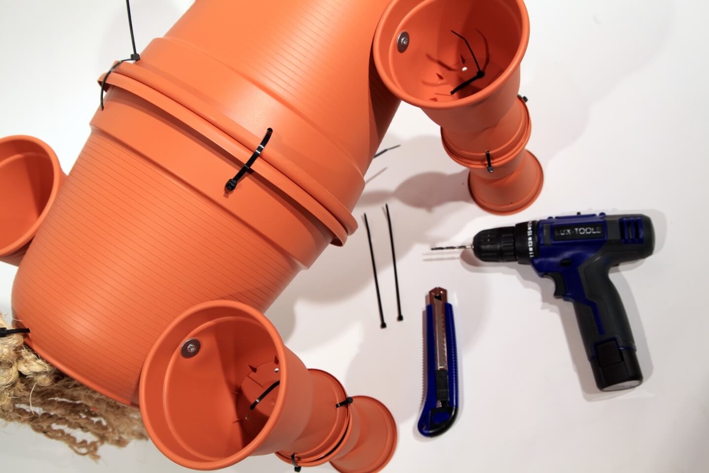 Akkuschrauber, Cutter und Kabelbinder liegen neben zusammengebauten Blumentöpfen