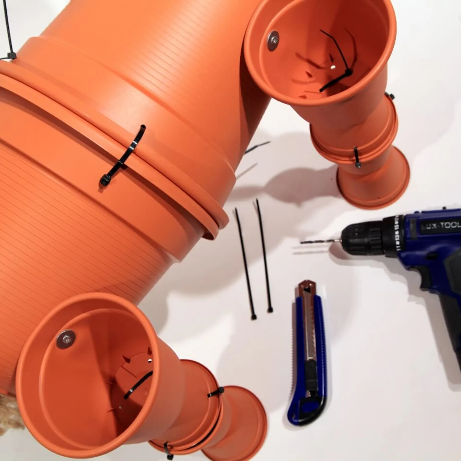 Akkuschrauber, Cutter und Kabelbinder liegen neben zusammengebauten Blumentöpfen