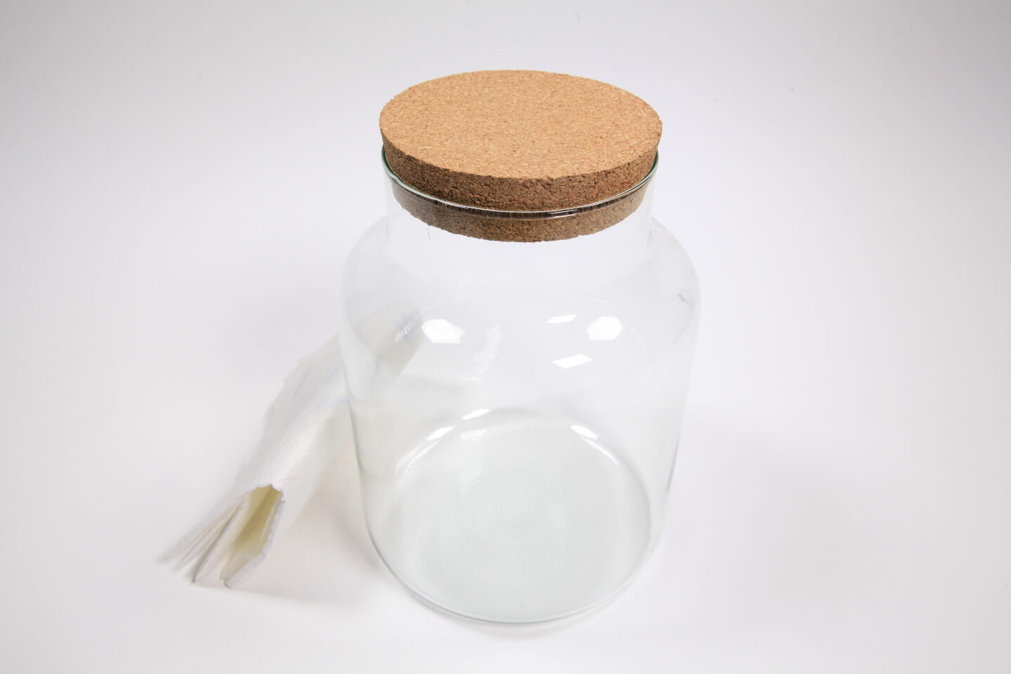 Na stole stojí prázdna sklenená nádoba s viečkom. Vedľa je utierka.