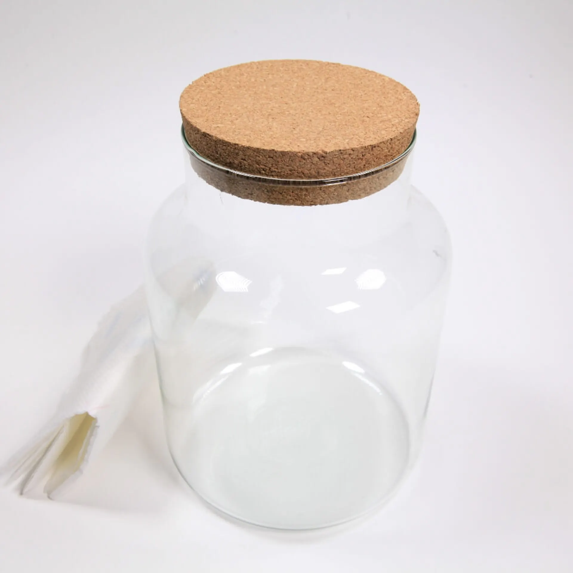 Na stole stojí prázdna sklenená nádoba s viečkom. Vedľa je utierka.