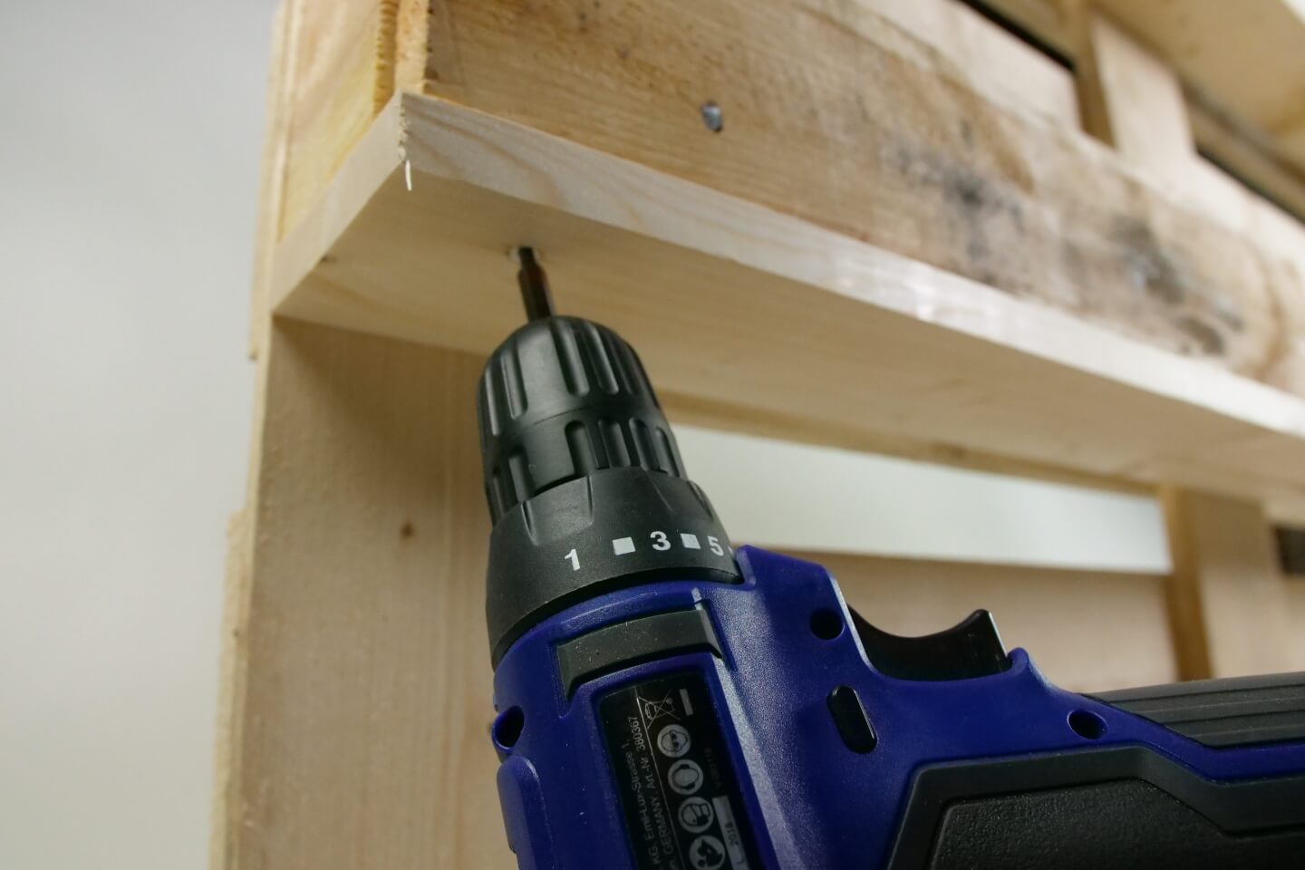 Es ist eine Nahaufnahme einer Holzpalette zu sehen. Mit einem Akkubohrer wird ein Brett an dieser befestigt.