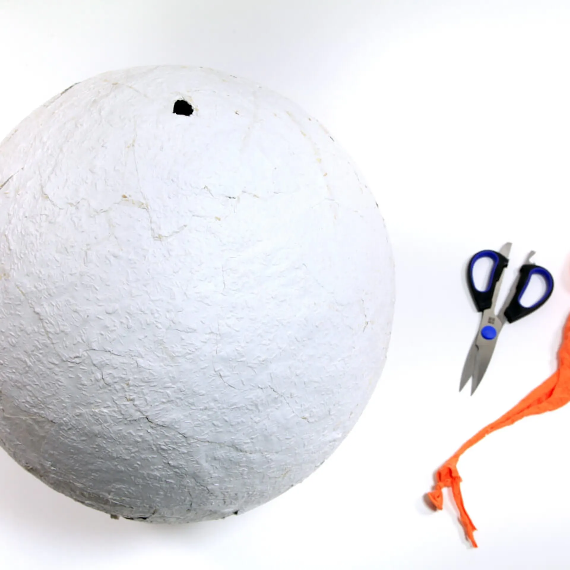 Neben der getrockneten Kugel liegen nun der luftleere Ballon und eine Schere, die den Luftballon zerschnitten hat.