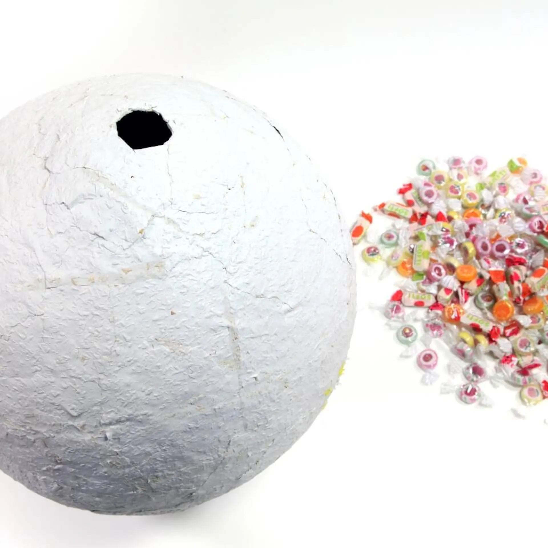 Die Piñata-Kugel hat nun ein größeres Loch, das du mit Süßigkeiten füllen kannst. Daneben liegen die Bonbons.