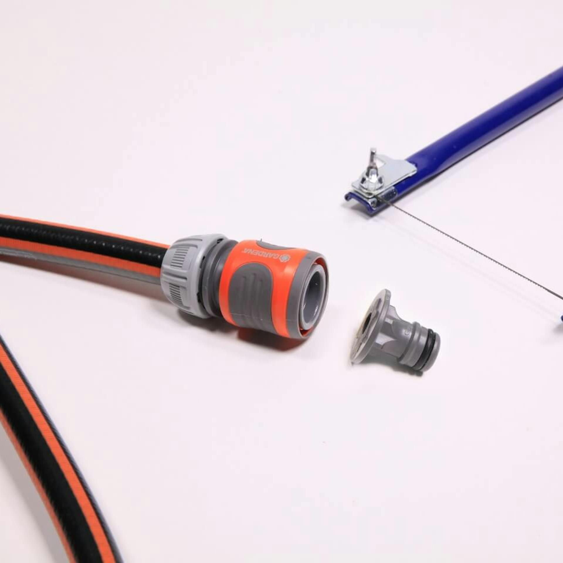 Ein Gartenschlauch, daneben liegen das abgesägte Schlauchventil und eine Laubsäge.