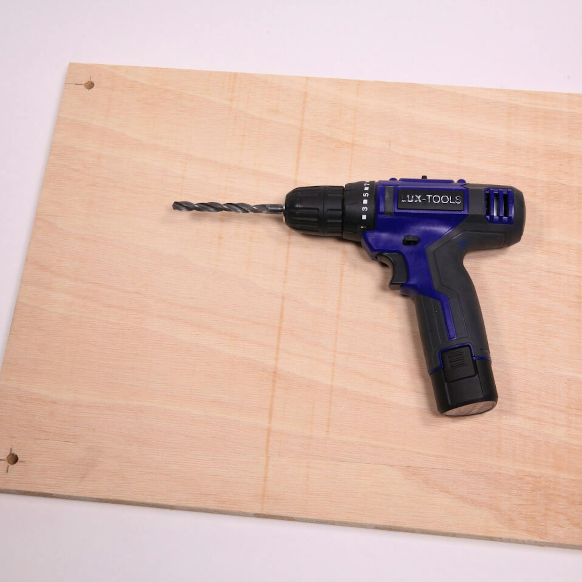 Eine Holzplatte mit zwei Löchern in den Ecken. Darauf liegt ein Akkuschrauber.