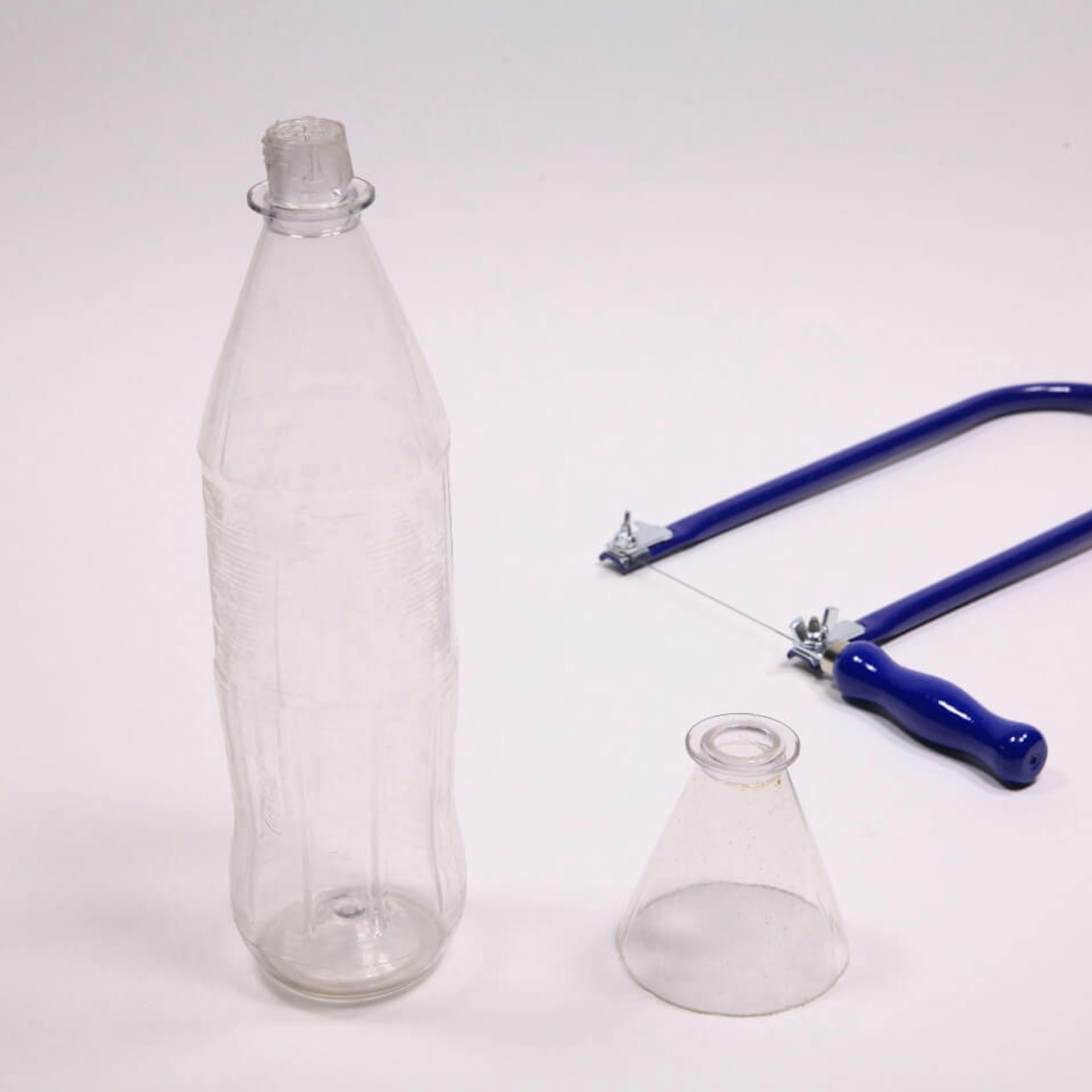 Eine Plastikflasche, daneben ein abgeschnittener Flaschenhals und eine Laubsäge.