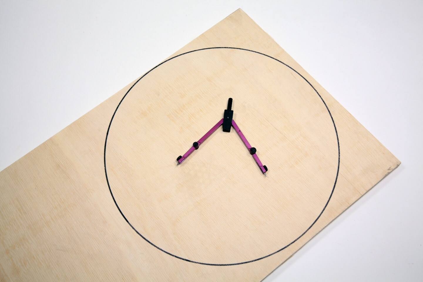 Zirkel liegt auf Holzplatte mit aufgezeichnetem Kreis.