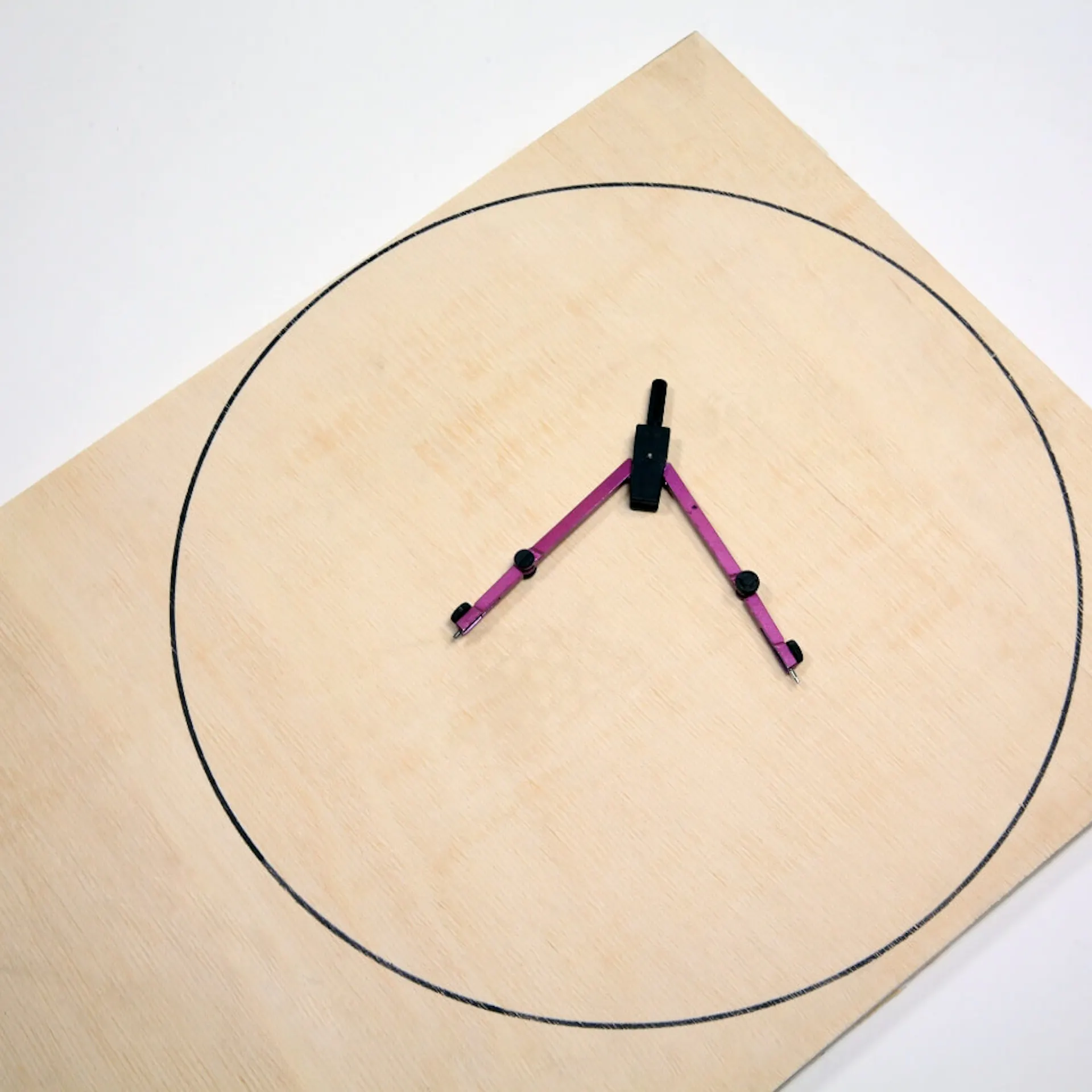 Zirkel liegt auf Holzplatte mit aufgezeichnetem Kreis.