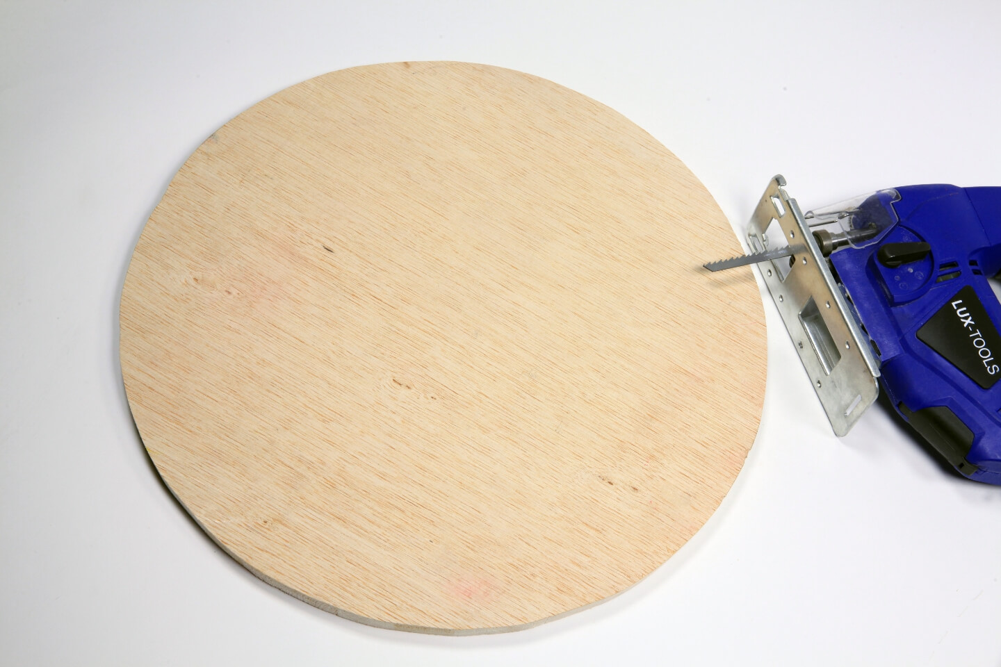 Stichsäge liegt neben runder Holzplatte.