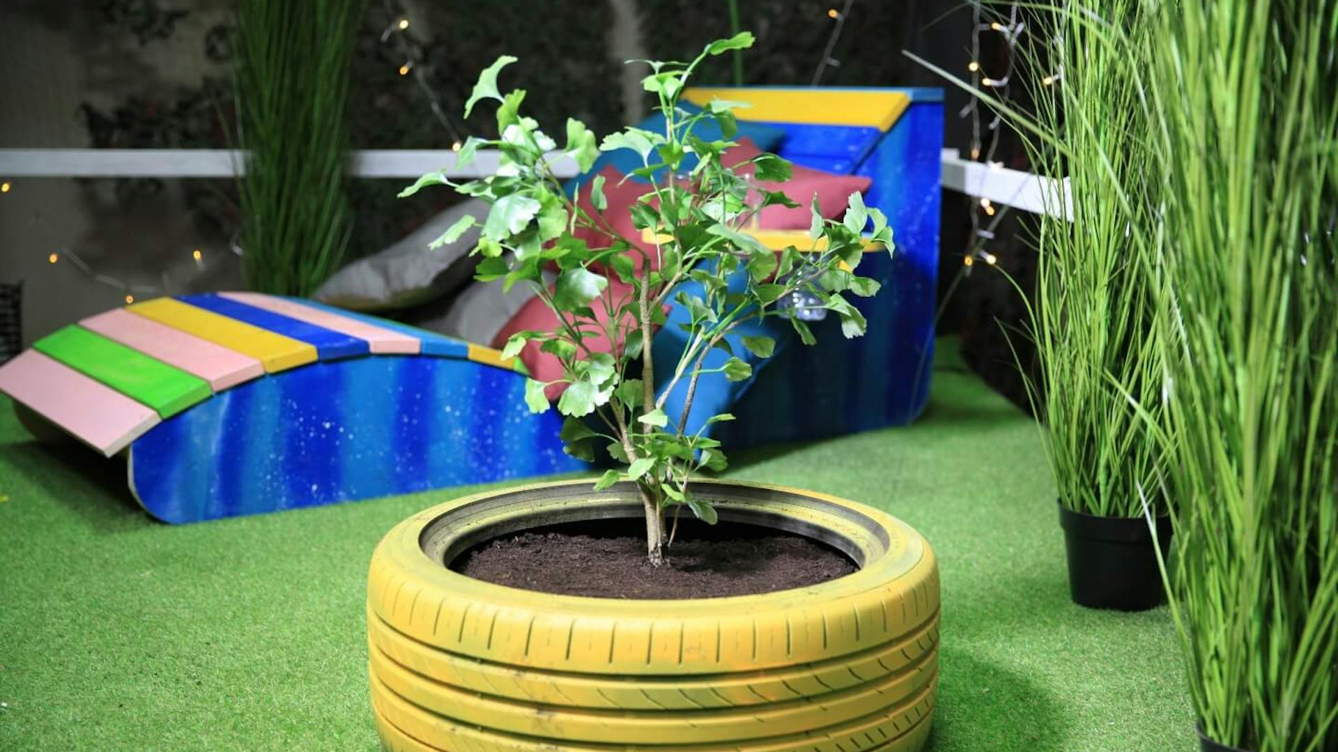 Gelb bemalter Autoreifen als Blumenkübel mit Pflanze und Erde