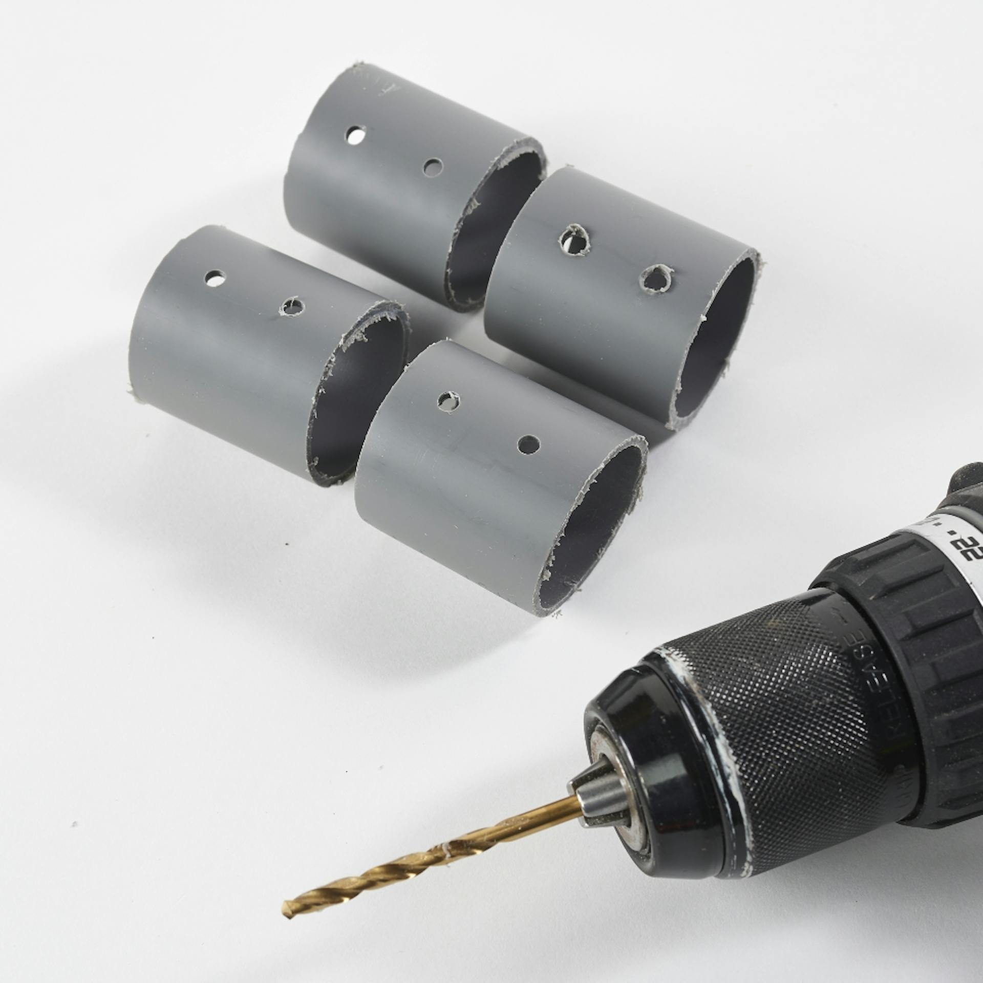 Vier Kunststoffrohr-Stücke mit Löchern liegen neben Akkuschrauber