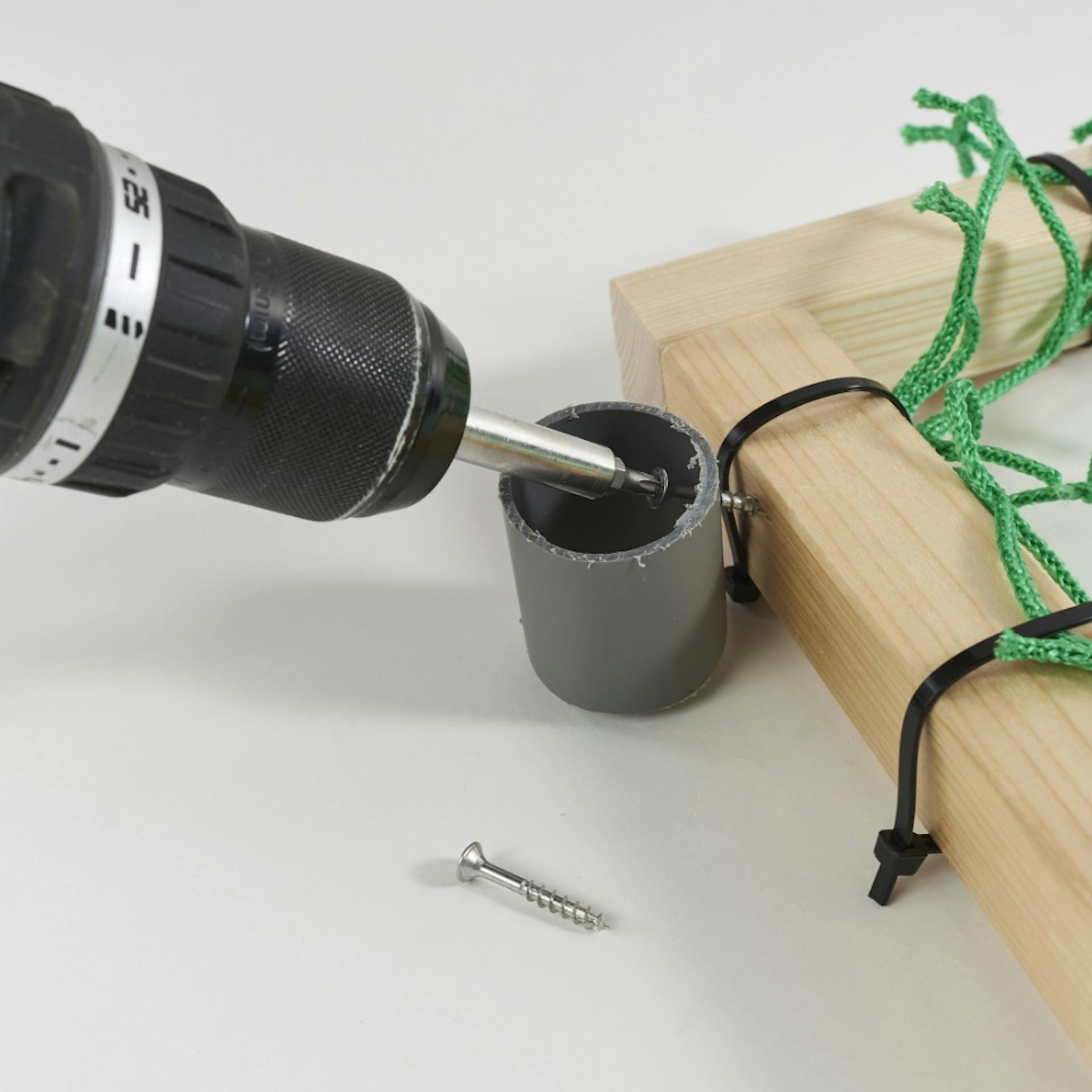 Akkuschrauber bohrt durch Kunststoffrohr an Kantholz