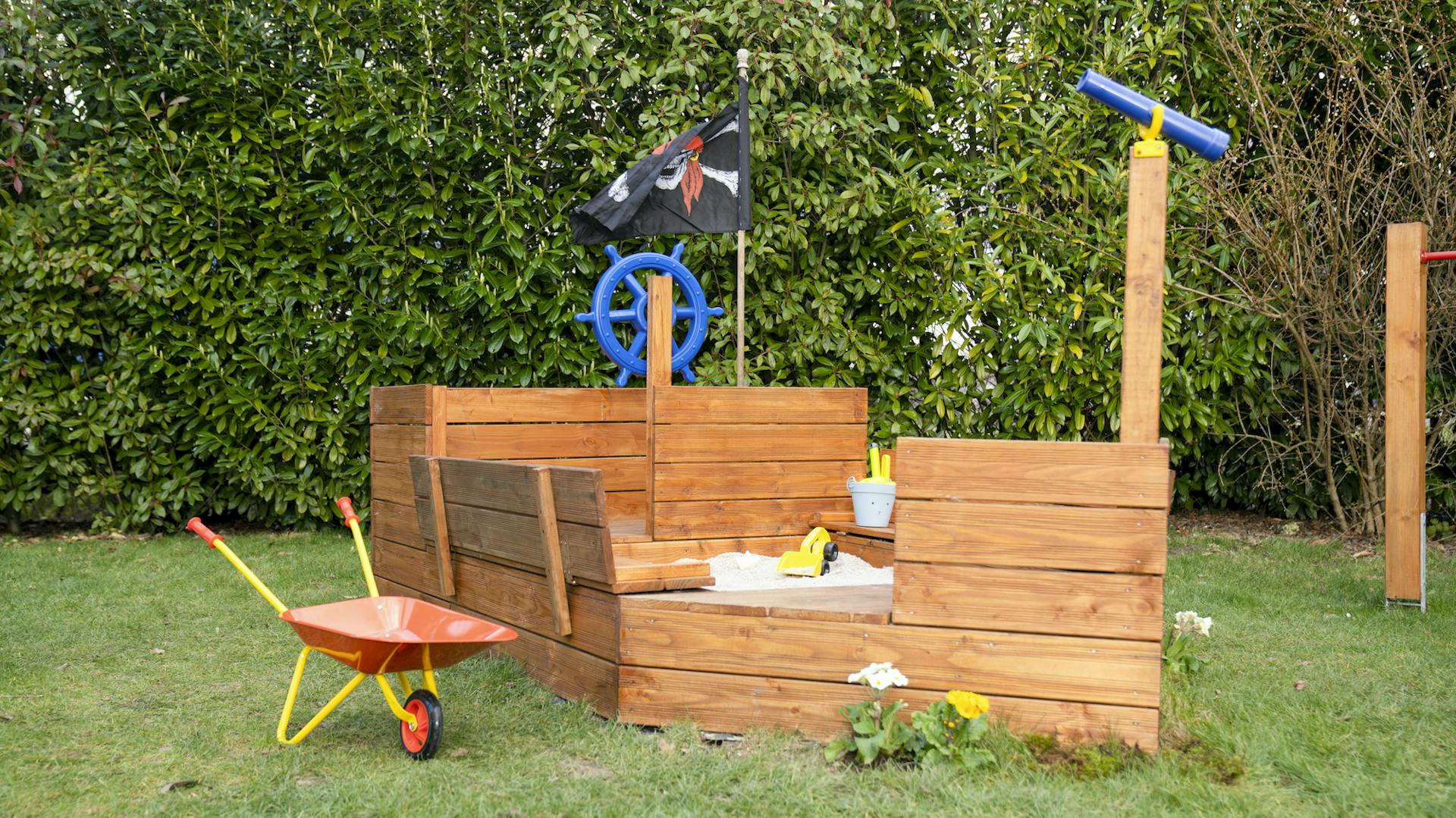 Sandkasten aus Holz in Schiffform auf Wiese